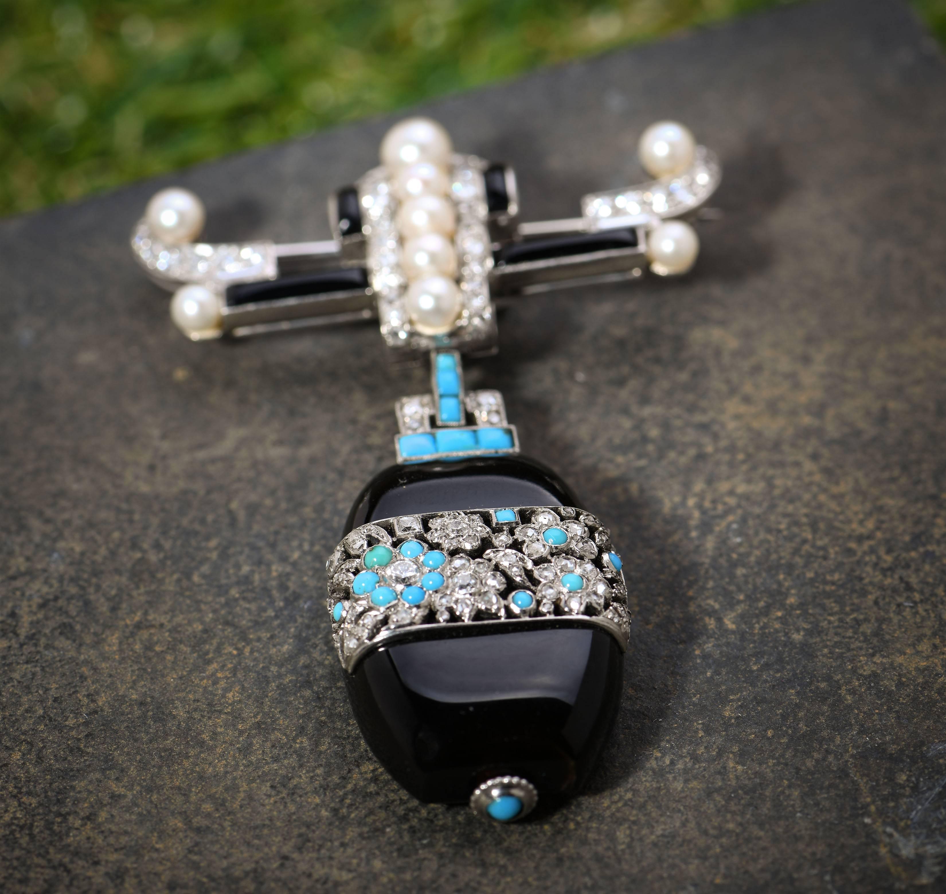 This is a fantastic example of 1920s jewellery design. It has the bold contrasting colours of onyx, pearls, diamonds and turquoise. It has the strong structure of Art Deco and the floral design of the Far Eastern influence so popular in the 1920s.