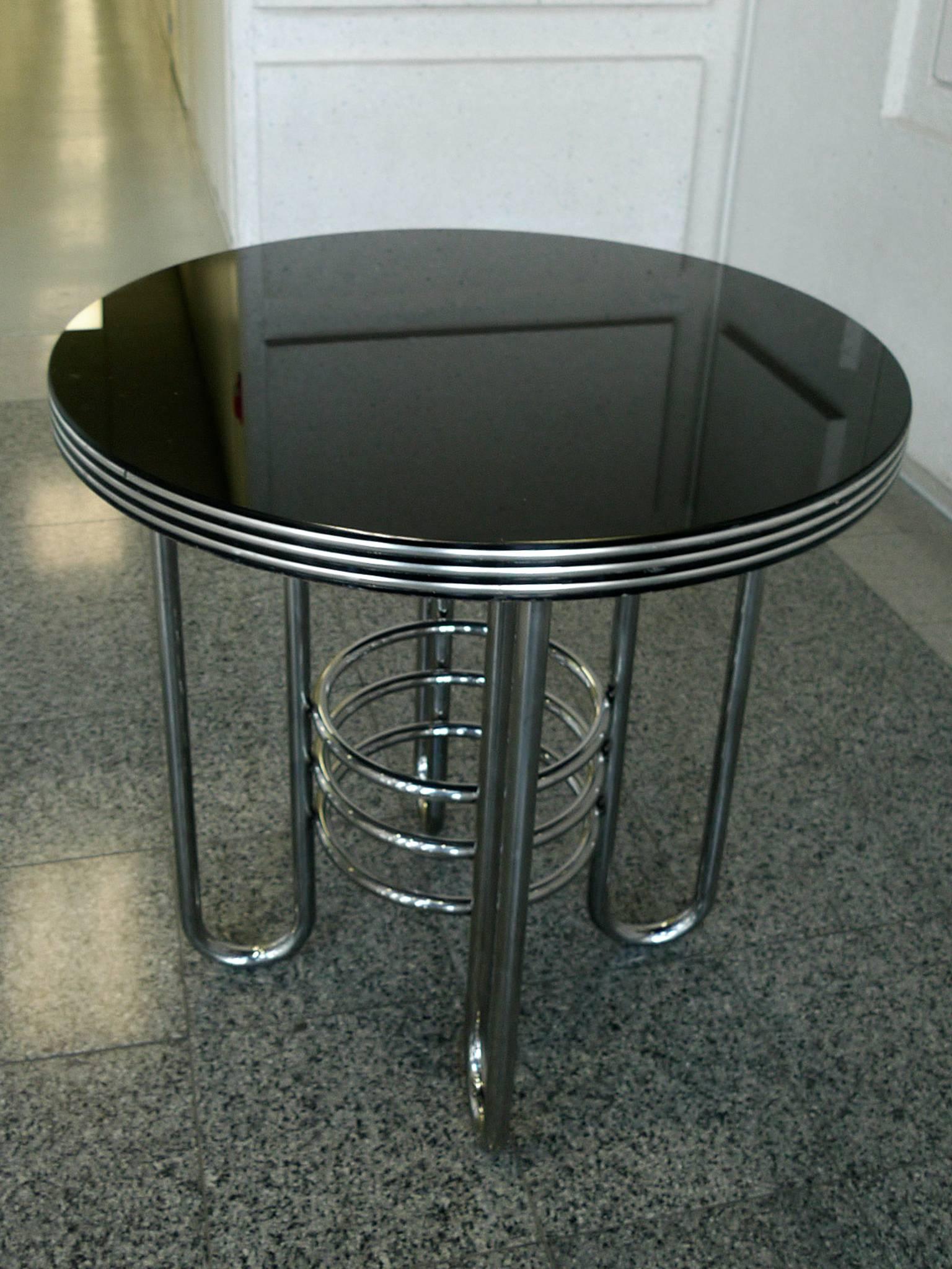 This round occasional table is in the Art Deco, Machine Age style. It's comprised of a tubular chrome frame and a black glass top. Like Gilbert Rohde's designs, the table distils the modern look of Industrial machines into a Minimalist, decorative