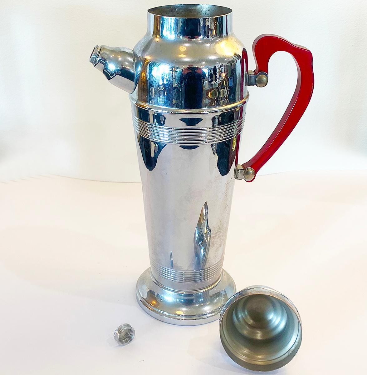 Art Deco cocktail set of lidded shaker stainless chrome as marked to base of 6 goblets and Shaker, translucent red Bakelite handle. Screw off pourer top inner strainer for pips or ice cubes, Stainless chrome base, cap chromed copper to tight fit