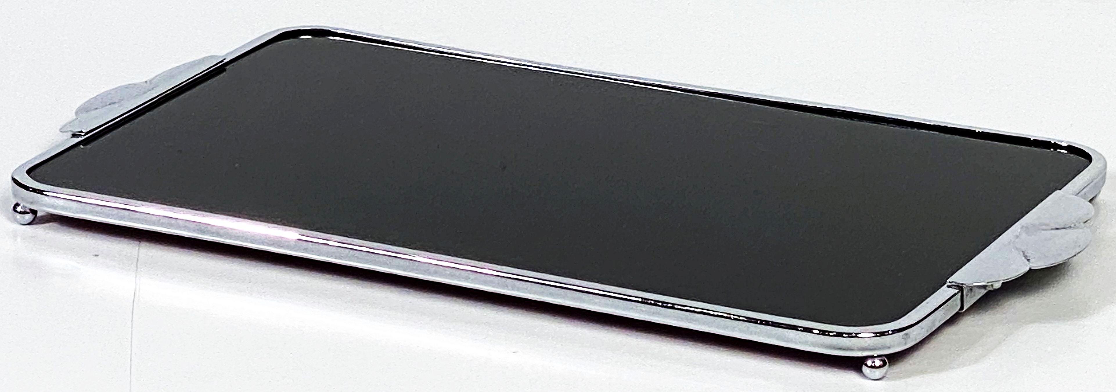A period Art Deco rectangular serving tray for drinks and cocktails from England, featuring two opposing handles and frame of chromed metal surrounding an inset black glass tray surface, resting on ball feet. Underside of cordovan pressed