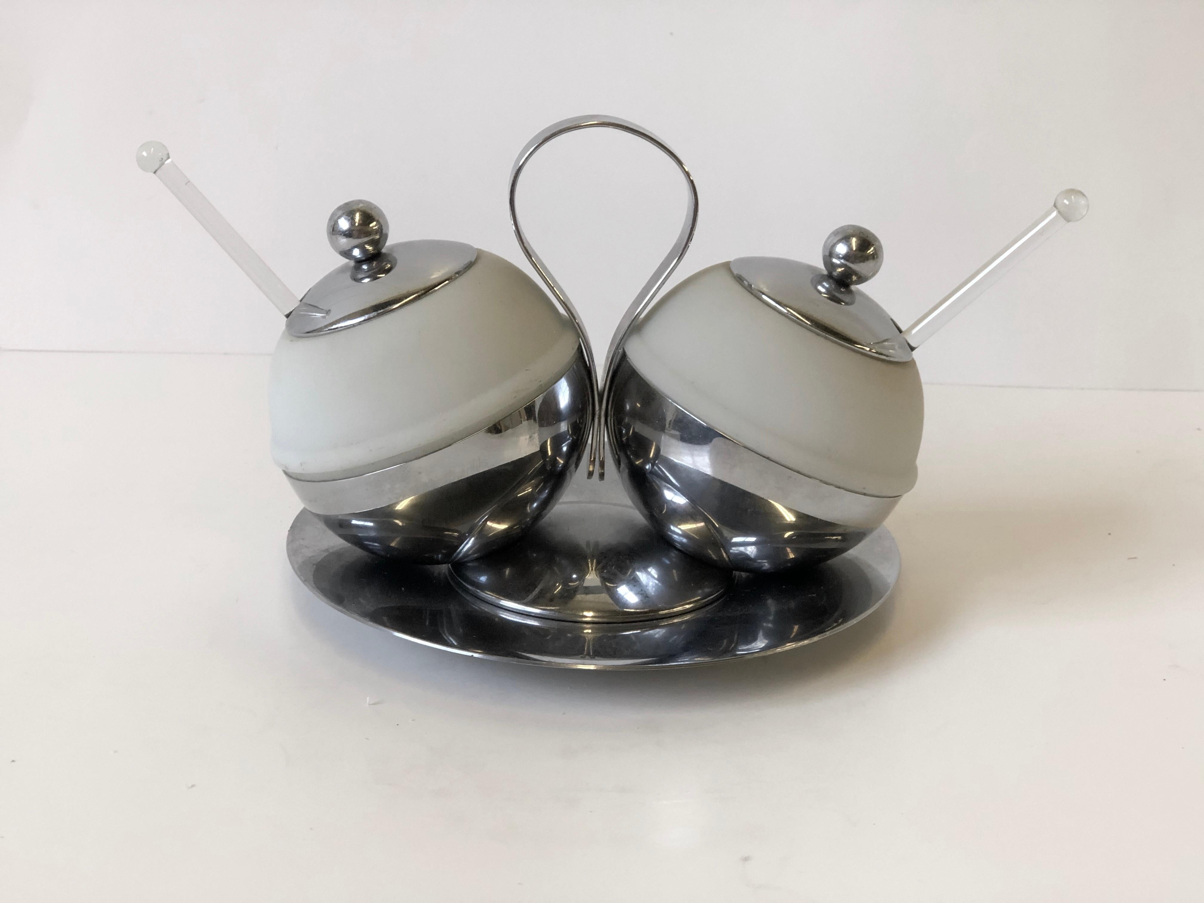 Rare 1930s Art Deco serving piece that could be used as a cream and sugar or salt and pepper set that is made of chrome and frosted glass. The set includes the lidded double server on stand, a plate rest, and a pair of glass spoons. The set was made
