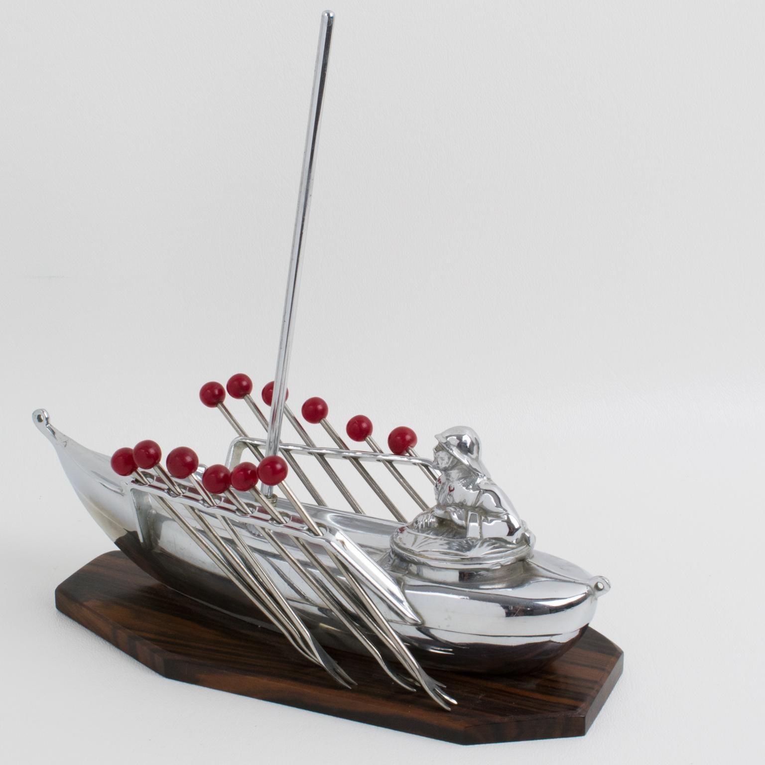 Dieses wunderbare französische Cocktail-Set zeigt ein Miniaturboot mit einem Matrosen. Zwölf Gabeln mit rotem Bakelit-Finial können von jeder Seite des Segelboots abgenommen und als Cocktail-Picker für Manhattans, Martinis oder andere Cocktails, die