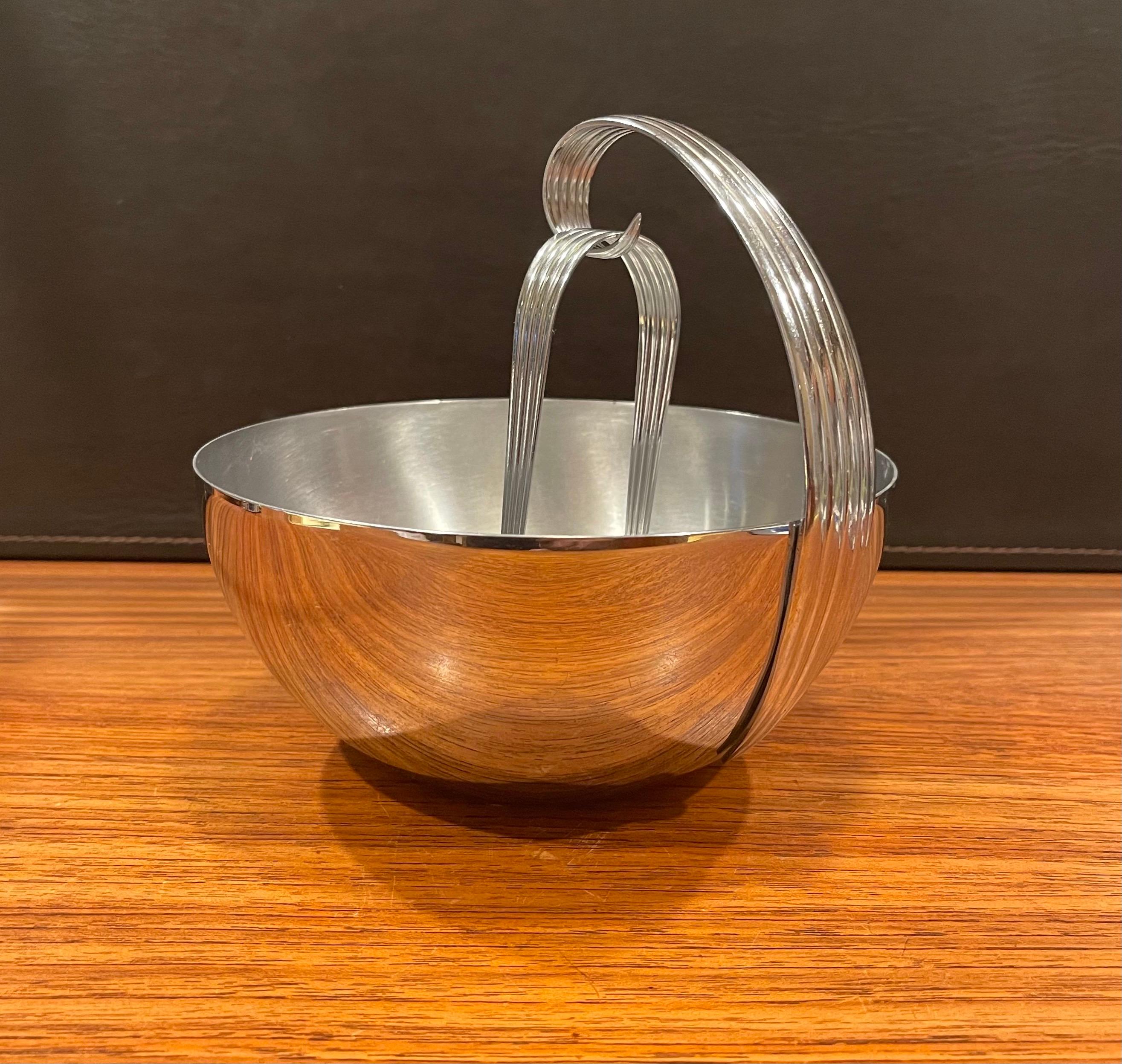 A very nice Art Deco chrome ice bucket with tongs by Russel Wright for Chase & Co., circa 1930s. The design features a ribbed and curved handle on a small stainless steel bucket or bowl. The set is in very good condition and measures 7