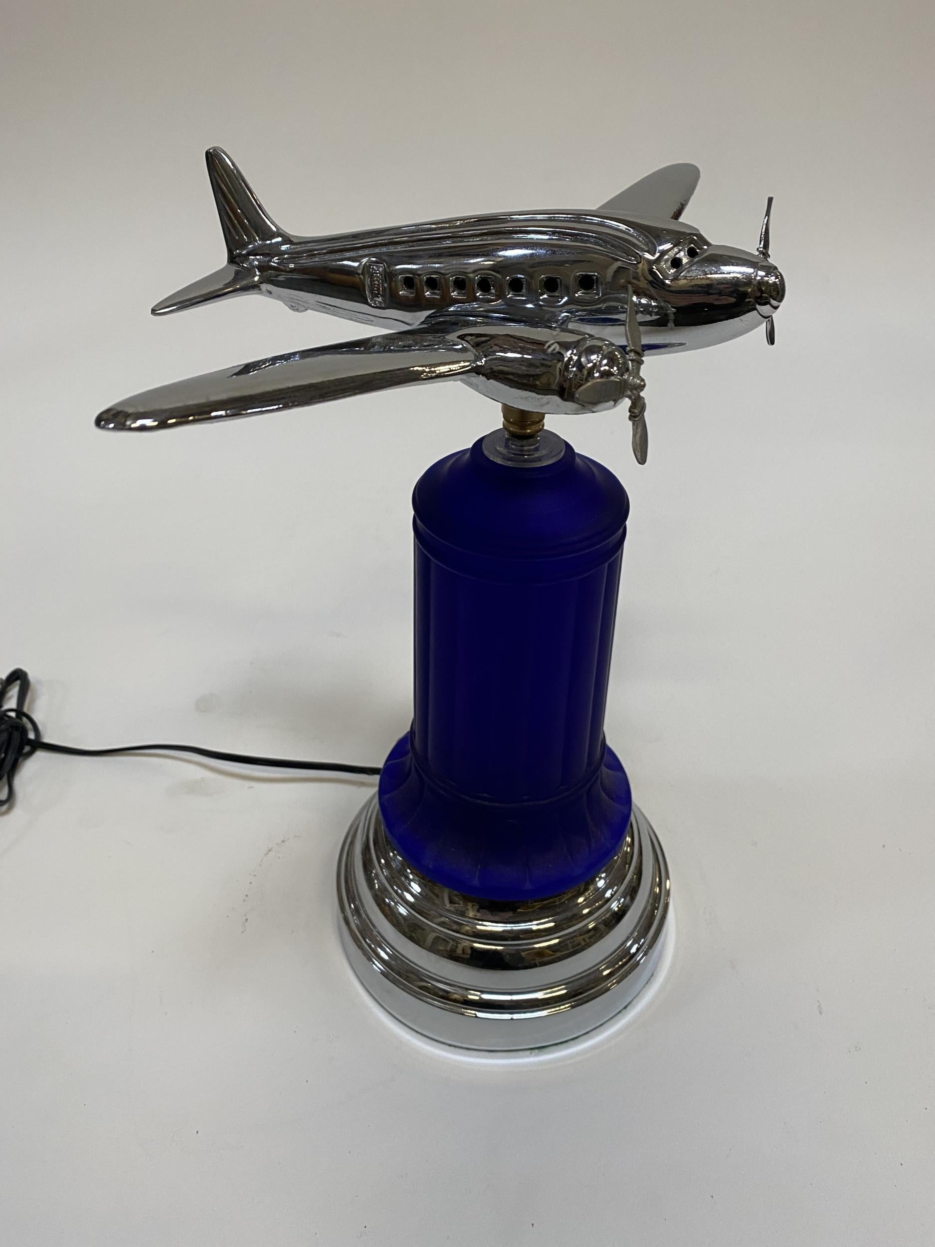 This custom chrome airplane accent lamp was created in Los Angeles in the 1980s using a re-edition 1930s cobalt glass table lamp. This 1930's inspired lamp features a cobalt glass light up center with an added chrome base and light up airplane model
