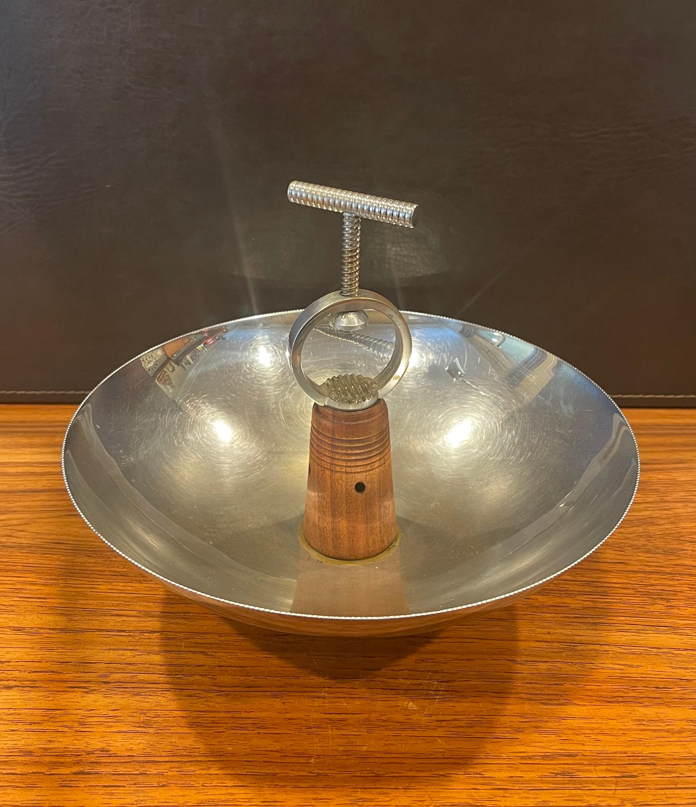 A very hard to find Art Deco chrome nut bowl with built-in screw cracker by Chase & Co., circa 1930s. The design features a solid walnut base and stem holding a round chrome bowl and metal hand screw cracker. The piece is in good condition; there is