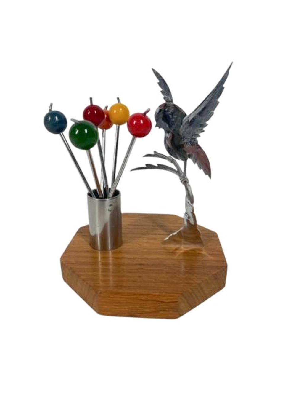 Juego de púas de cóctel Art Decó con una figura cromada de un pájaro que se posa en un árbol sobre una base octogonal de madera junto a un cilindro cromado que sostiene seis púas de cóctel bifurcadas, cada una rematada con una bola de baquelita de