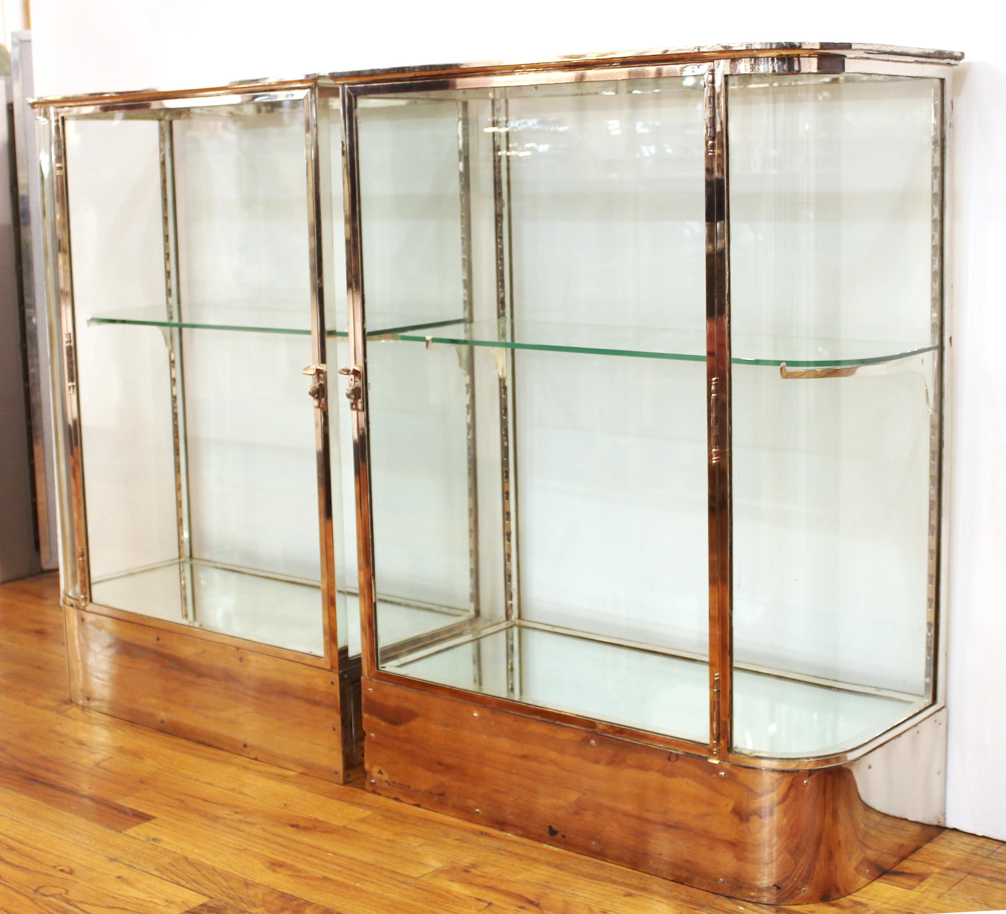 American Art Deco period pair of glass display cabinets in chromed metal with one glass shelf each. Each cabinet has one rounded corner on opposite sides and a mirrored bottom shelf. Minor age-related wear and surface scratches to the chrome. Minor
