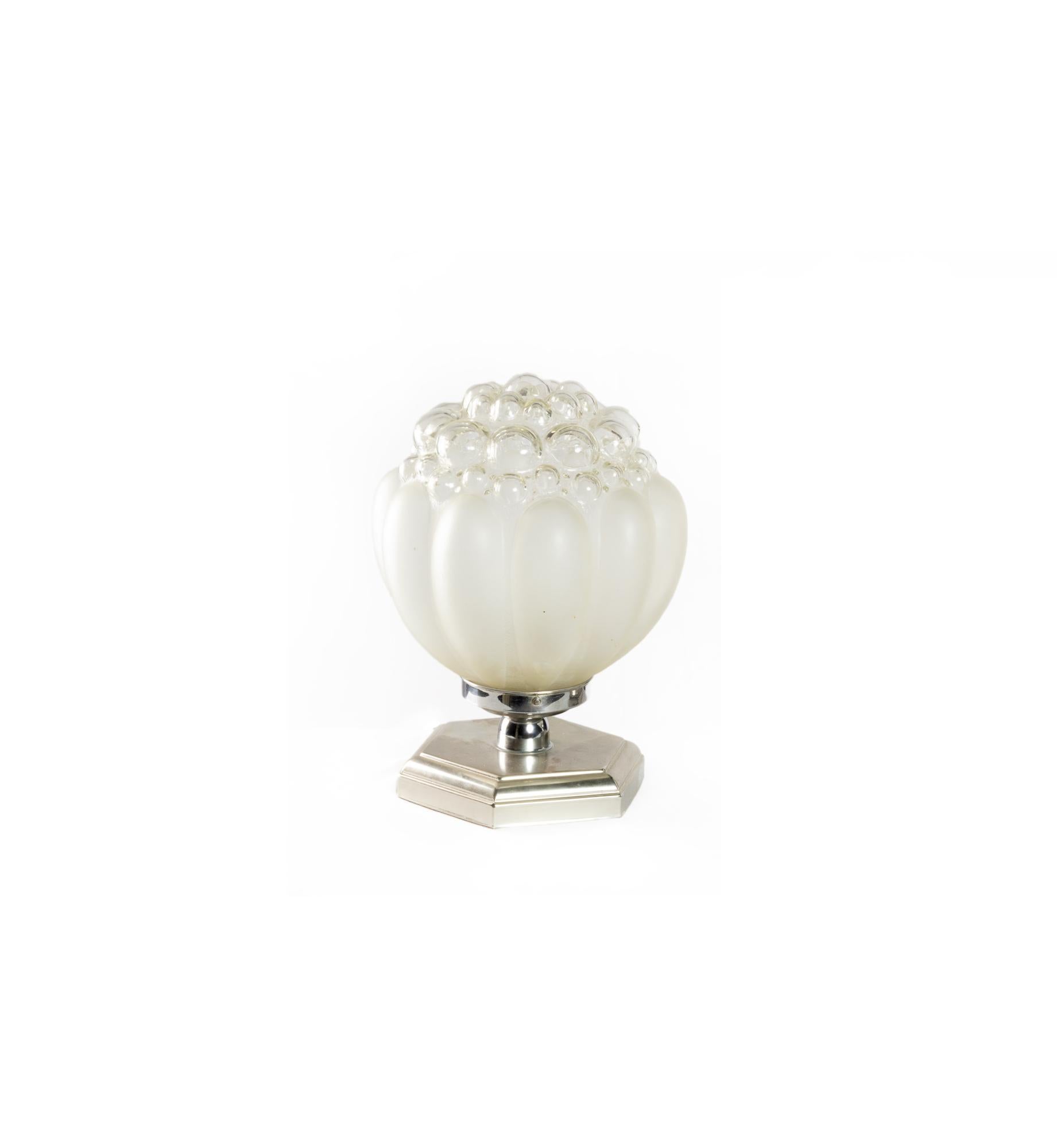 An elegant Art Deco table lamp with blown glass shade and polished chrome hexagonal base.

The blown glass shade has a pearlescent (nacre-like) finish that softly catches the light, creating a warm and sophisticated glow.

Its hexagonal base in