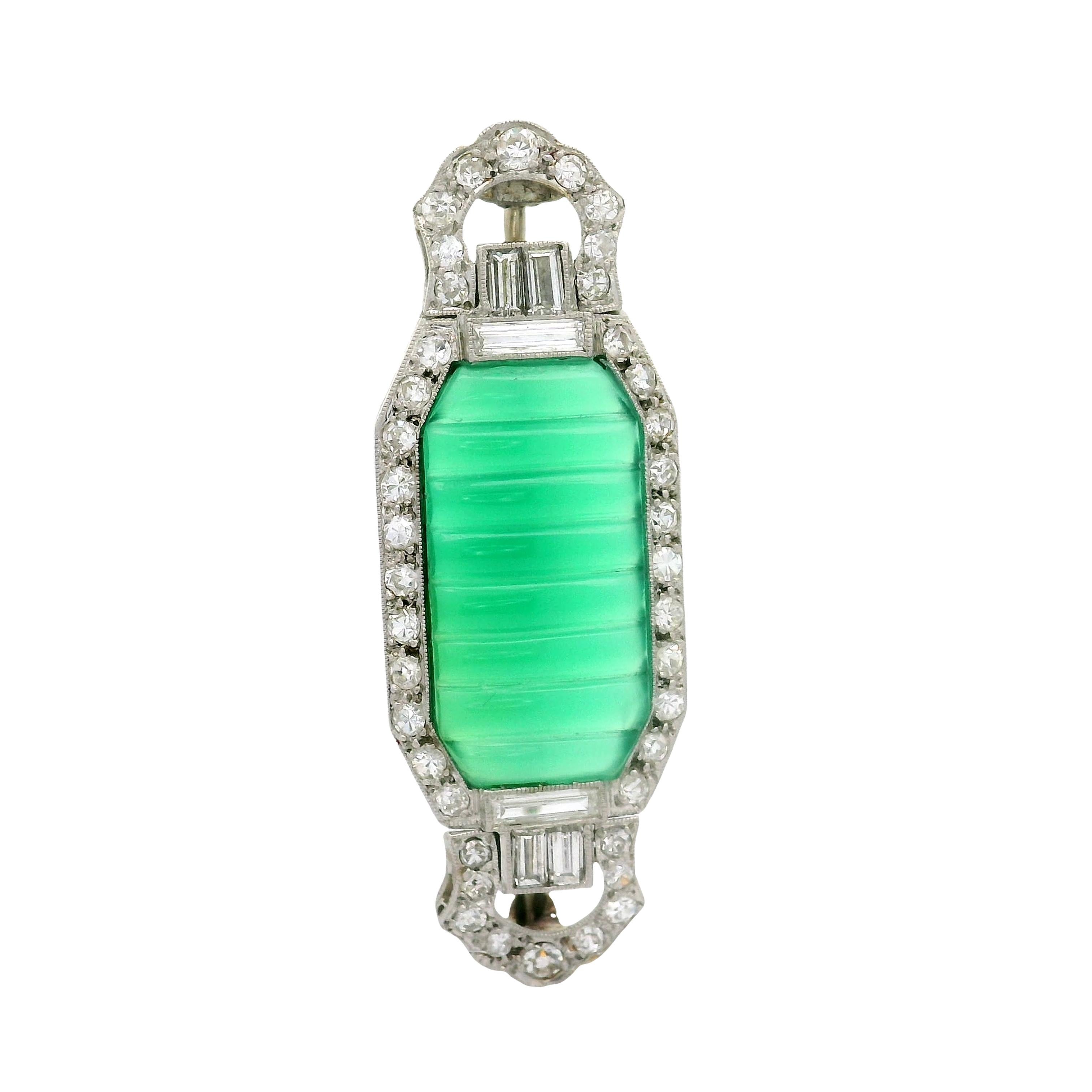 A striking Art Deco brooch featuring a carved-ribbed green chrysoprase as the focal point. The chrysoprase is elegantly framed by round-baguette white diamonds, adding a touch of sparkle. Crafted in platinum during the late 1920’s, this piece