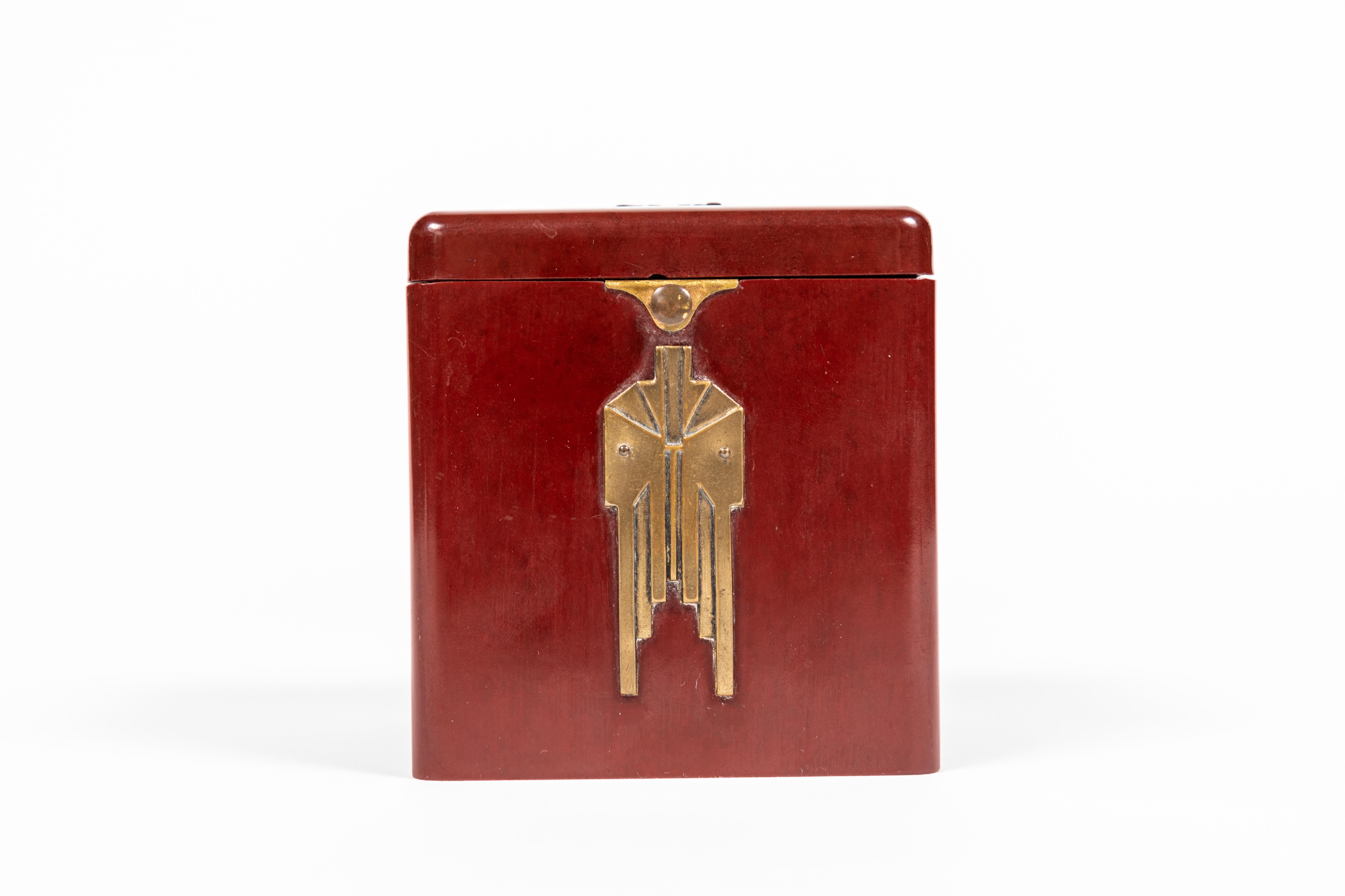 Art Deco burgundy square Bakelite box with period brass detailing. Interior has room for twenty-four cigarettes and has a button triggered hinged lid.

  