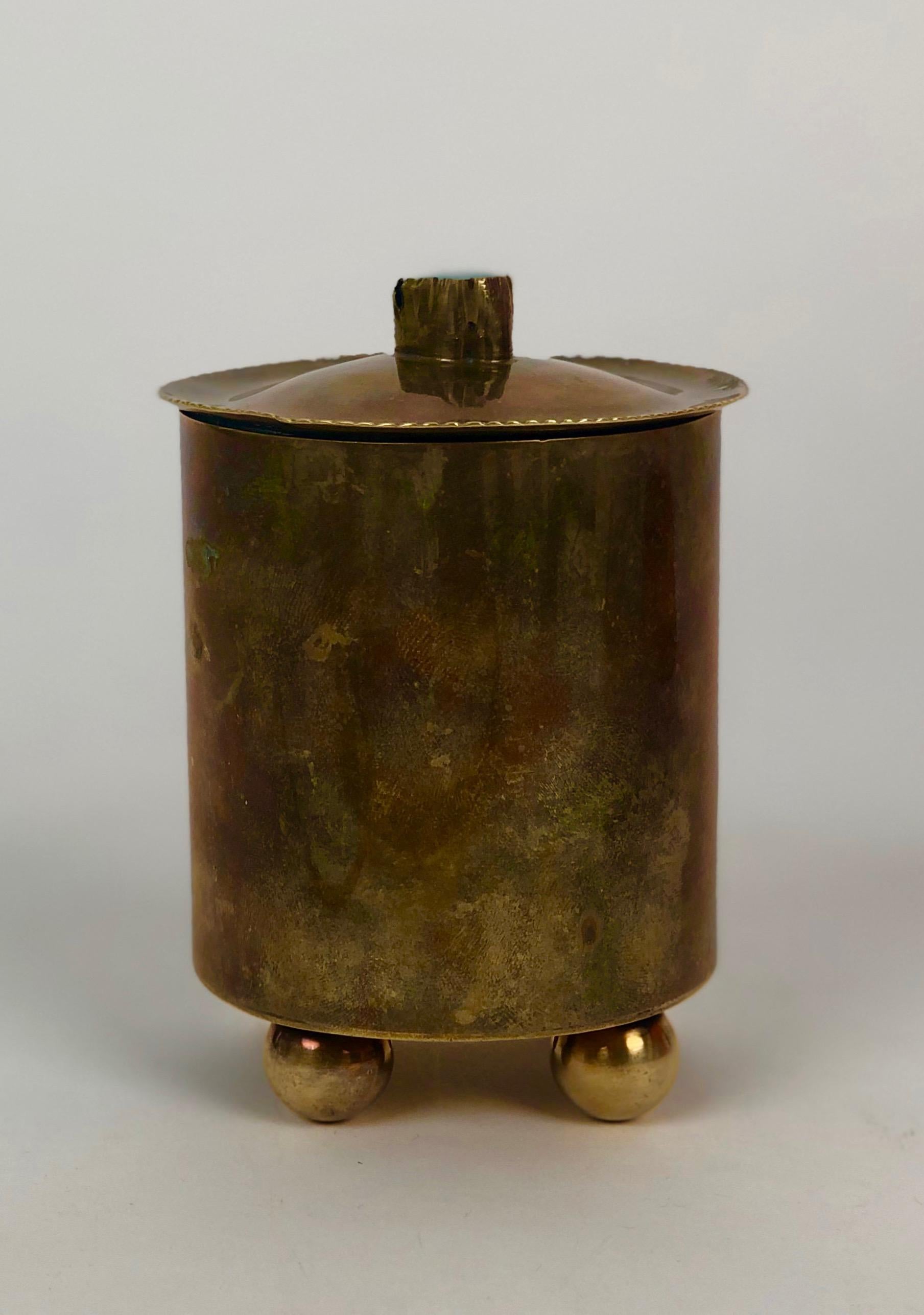A unique brass cigarette container from the 1920's hand made in Austria.
On top of the lid is a glass stone in turquoise colour. the lid fits tightly into the container.
From the bottom is visible  the makers mark but i found it difficult to read.