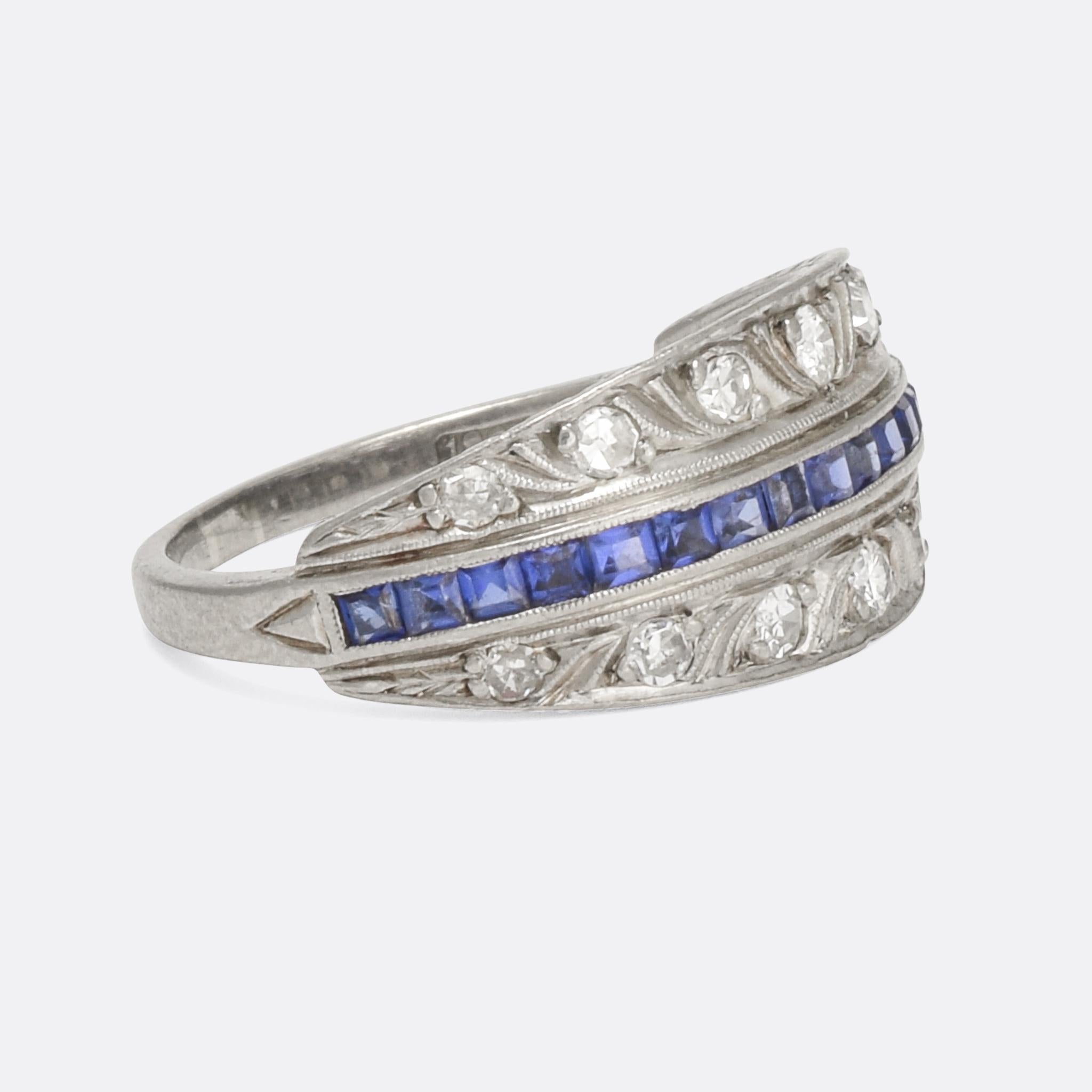 A stylish Art Deco cluster ring, set with a central seam of blue sapphires with seven graduated diamonds to either side. There are interesting details punctuating the whole head, with millegrain lines and curves, and triangle accents to the