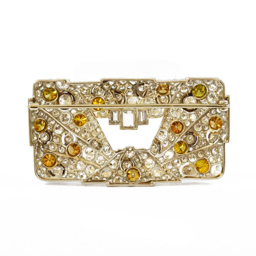 An Art Deco rectangular plaque brooch with open central panel. Pavé set with diamonds and cognac and sherry coloured diamonds, with intermittent rings of onyx framing some diamonds. Mounted in platinum. French, circa 1930. 