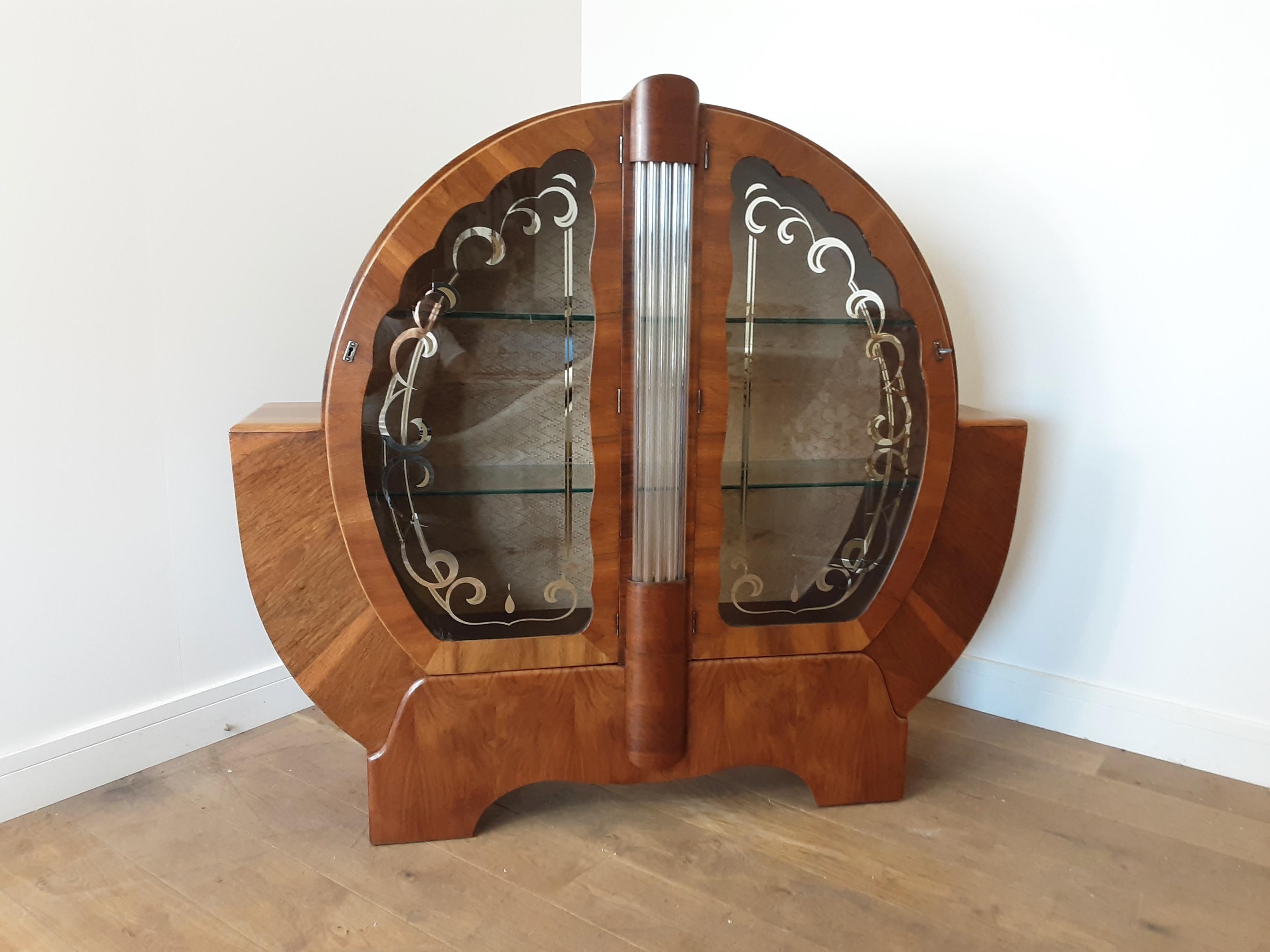 An Impressive Art Deco circular display cabinet in walnut with shouldered sides and silvered design to the glazed doors, central column of glass rods.
Measures: 126 cm H 135 cm W, 31 cm D
British, circa 1930.