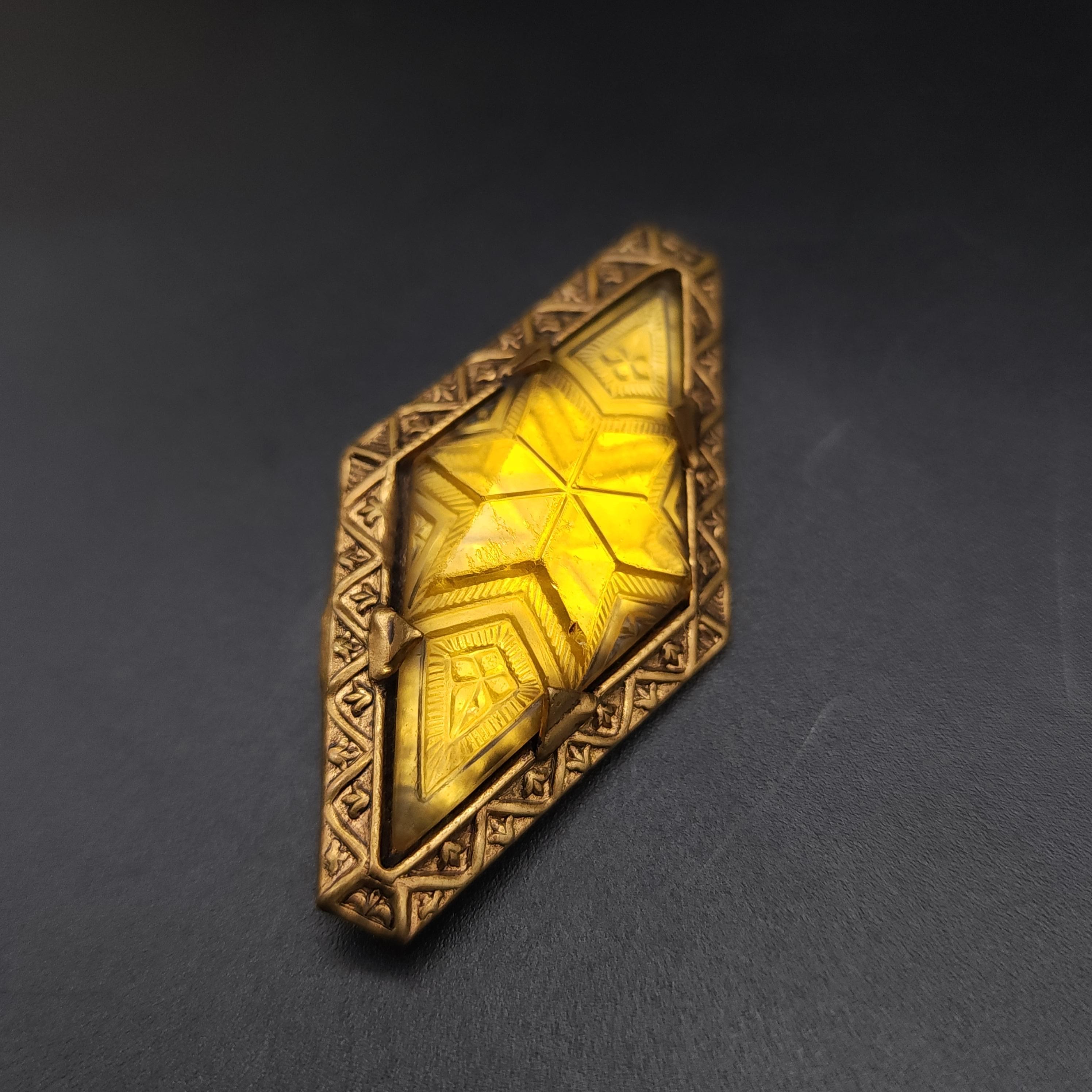 Size: 2 1/8 x 1 1/8 inches

Elevate your ensemble with this Art Deco vintage pin, featuring a gold-tone frame that exudes classic elegance. At its heart lies a dazzling citrine-colored crystal, prong-set and intricately carved with geometric designs