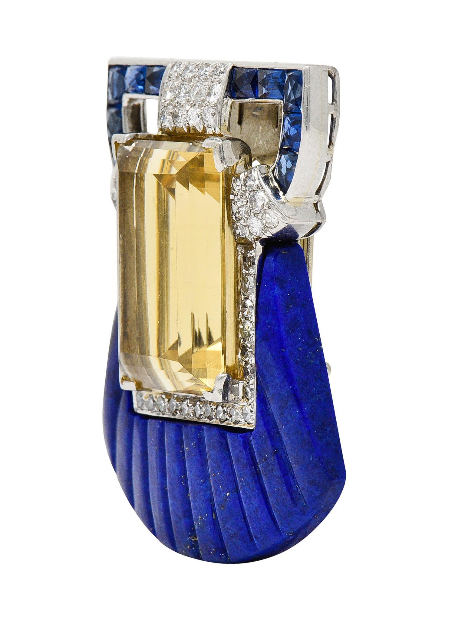 Brooch clip is formed as a stylized scallop shell

With deeply fluted and carved flanges of lapis lazuli

Opaque with strong ultramarine blue color with mild mottling and some gold pyrite flecks

Centering a rectangular cut citrine measuring