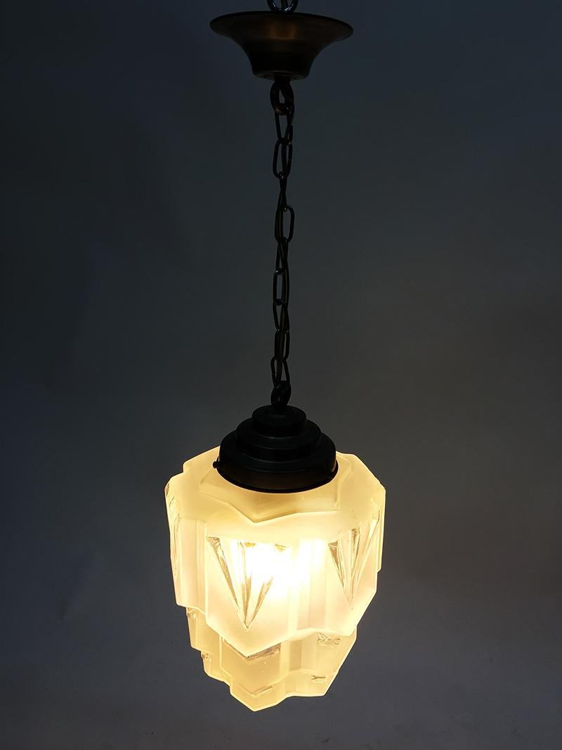 Art Deco clear and mat glass skyscraper pendant light 

Art Deco pendant light with a shade made of clear and mat glass 

1930s 

The measurements are: 

Total height 62 cm 
Approximate 20 cm diagonal 
The shade is approximate 28 cm high.