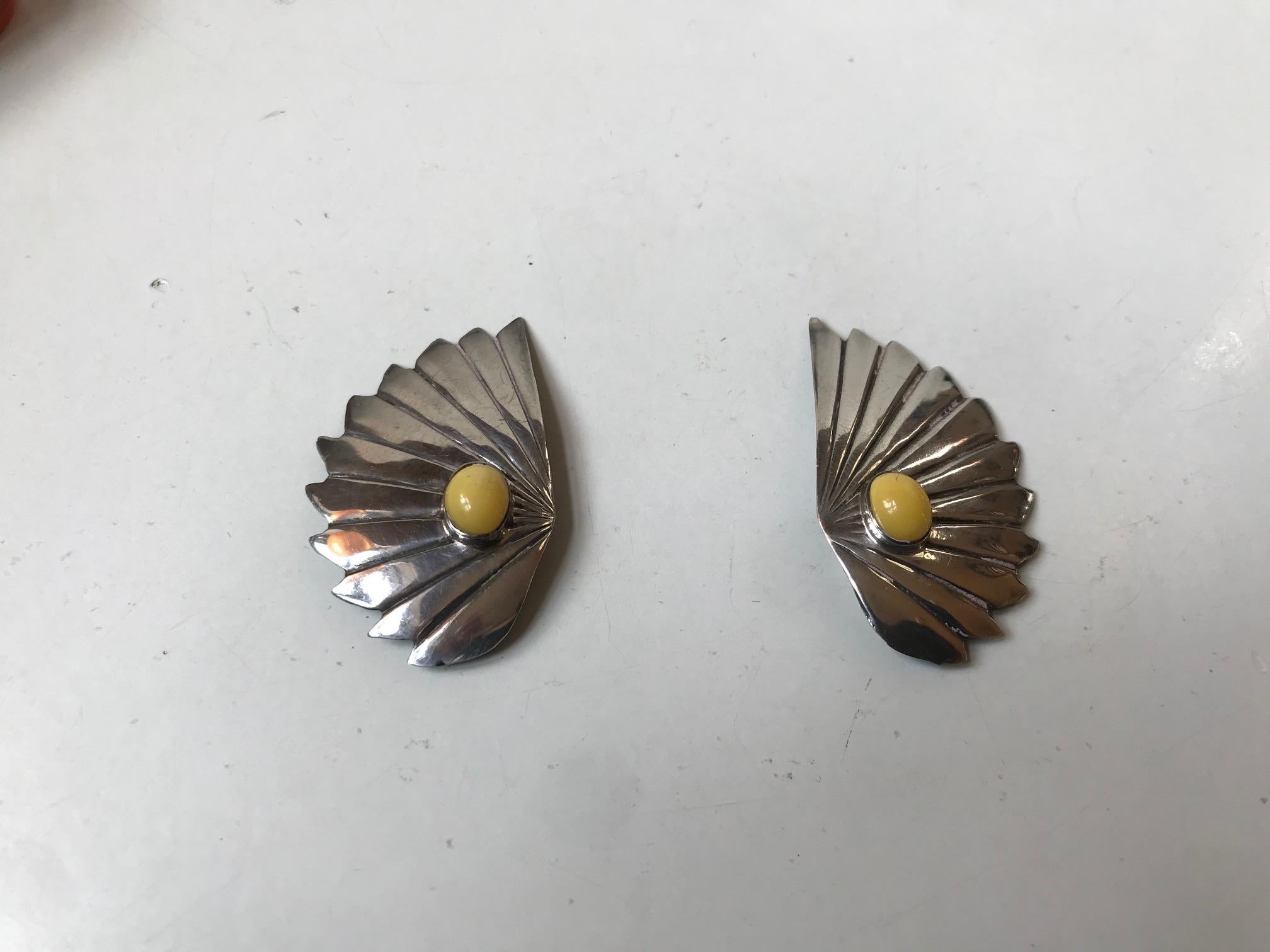 A pair of highly stylized clip-on earrings made from 830/1000 silver and set with yellow jade stones. Anonymous French silversmith circa 1925 in the style of Pierre Turin. Depicting angel wings this set is an example of the Devine Art Deco style