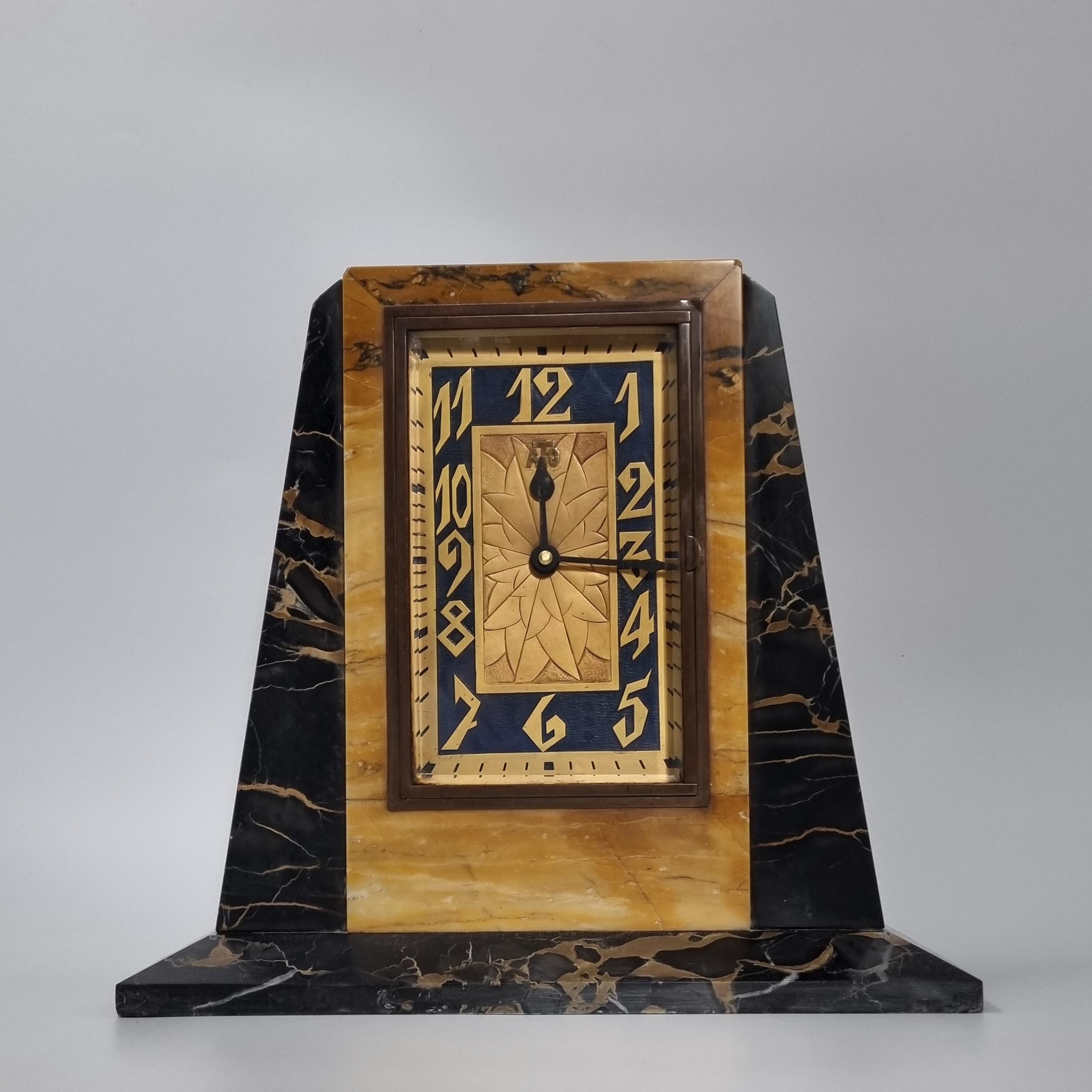 An Art Deco Clock, circa 1925 of footed rectangular form with graduated sloping sides, in two colours of marble, with metal clock face decorated with spiders web to the centre and embellished with stylised numbers against a enamelled blue ground,