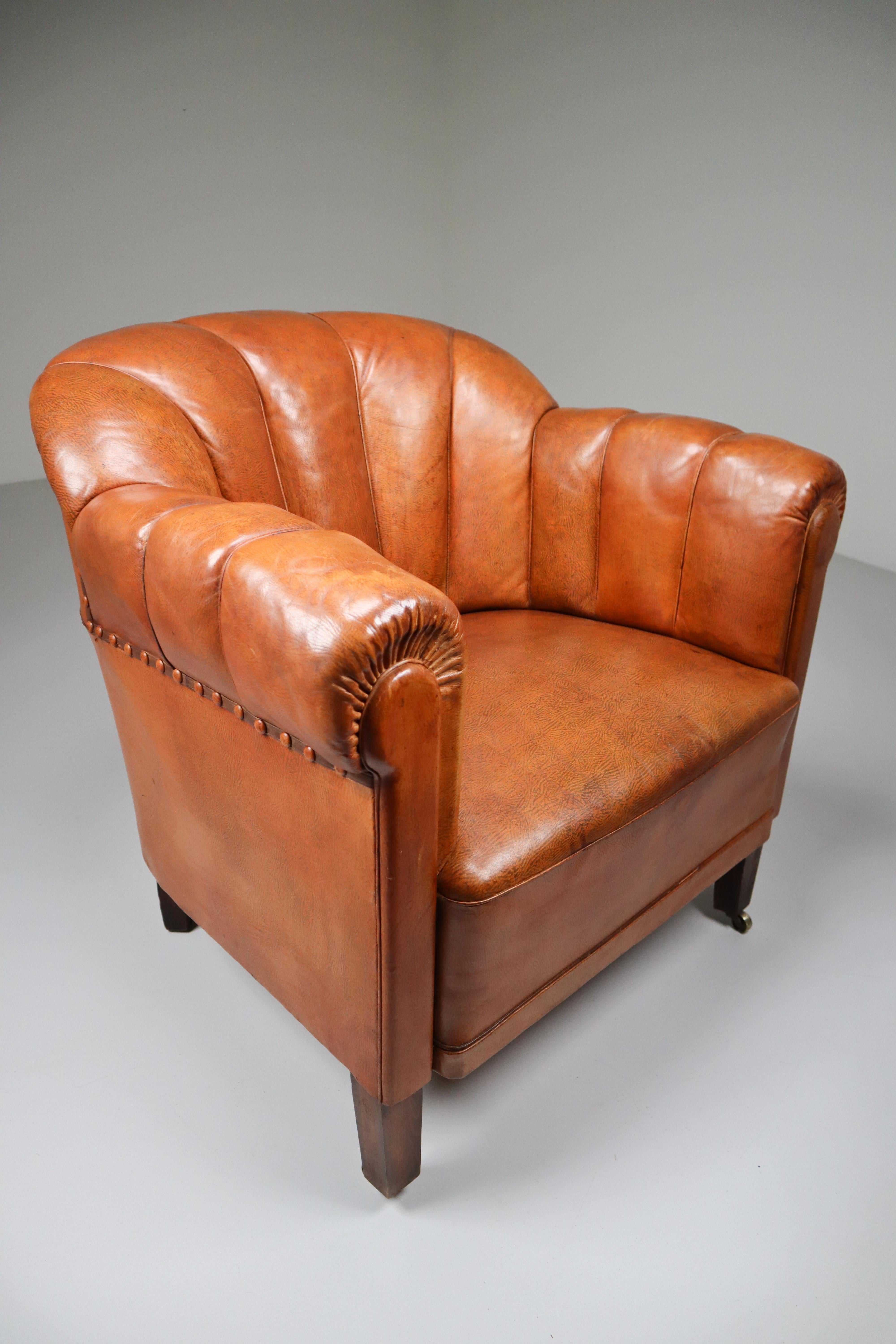 Art Deco club chair in absolutely gorgeous patinated cognac leather and feature metal rivets and wooden legs. The leather is beautifully patinated during use and age, in very good original condition. Prague, 1930s.