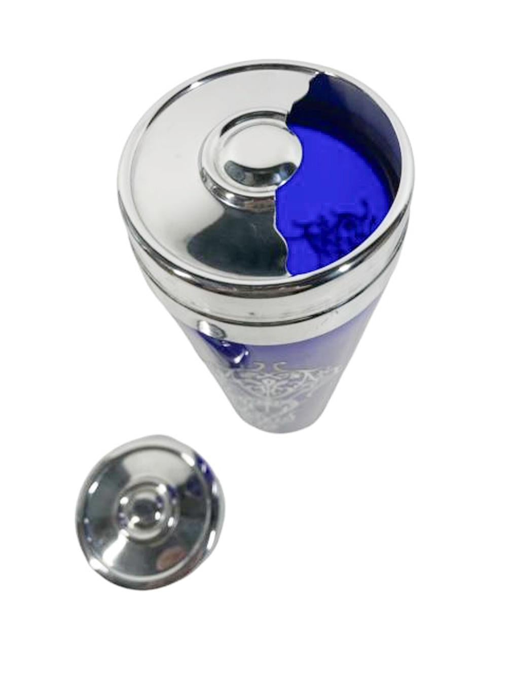 Coctelera Art Decó de vidrio azul cobalto con paneles de plata de ley de estilizadas enredaderas y hojas en tres lados y conectados por zarcillos simples. La tapa cromada en dos partes con colador integral y abertura para utilizarla como jarra de