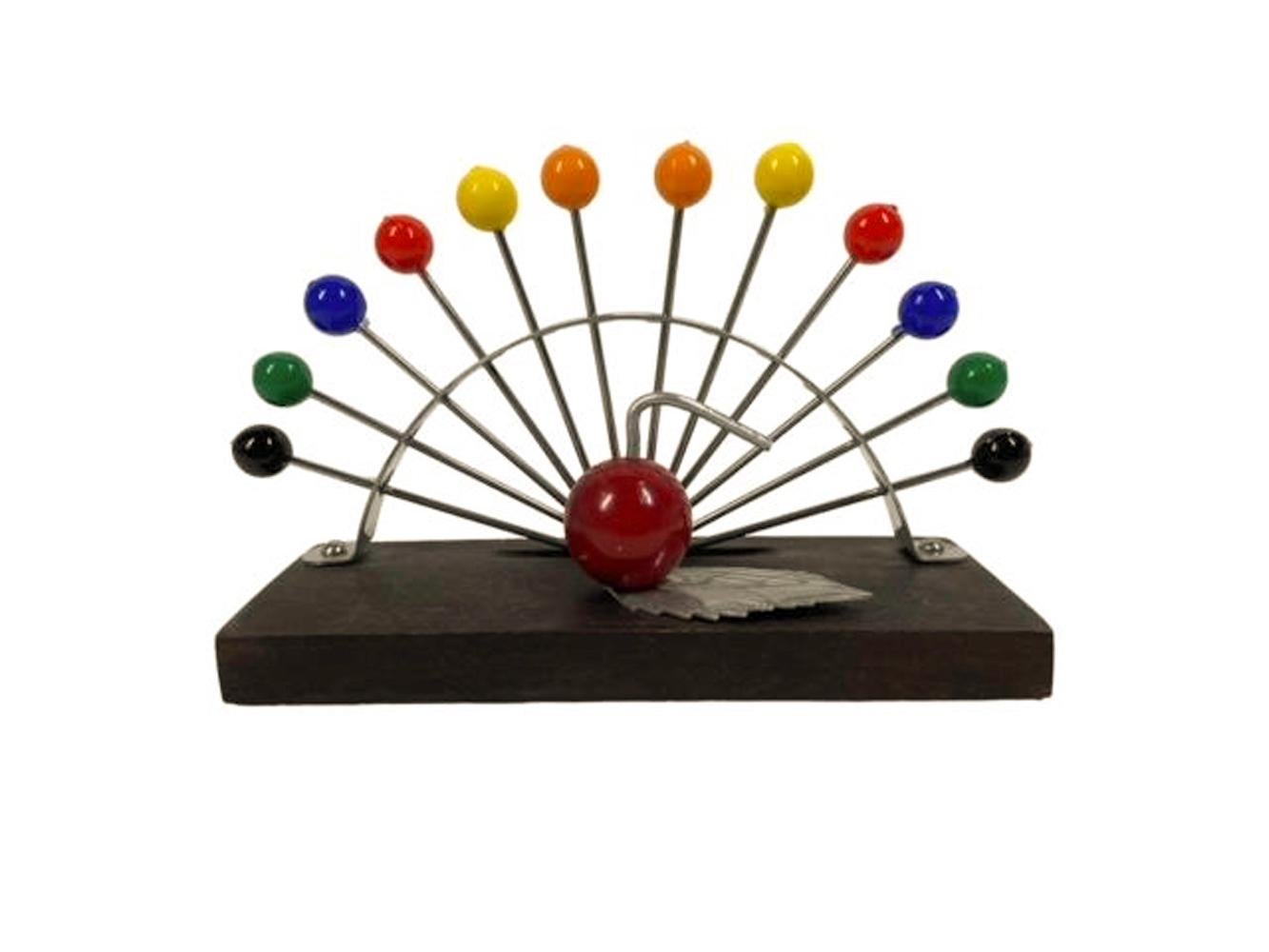 Ensemble de 12 pics à cocktail Art déco français (2 de chaque couleur), accompagné d'un support comportant une pomme en bakélite rouge et chrome sur une base en bois devant un arc en métal perforé qui maintient les pics en arc de cercle.