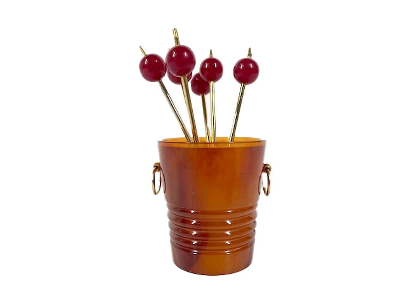 Art Deco cocktail pick set, 6 gilded picks with cherry red Lucite tops and forked ends in a holder of pail or flowerpot form made of tortoiseshell Bakelite with gilded ring handles. The bottom of the pail stamped in gold with an atomic model diagram