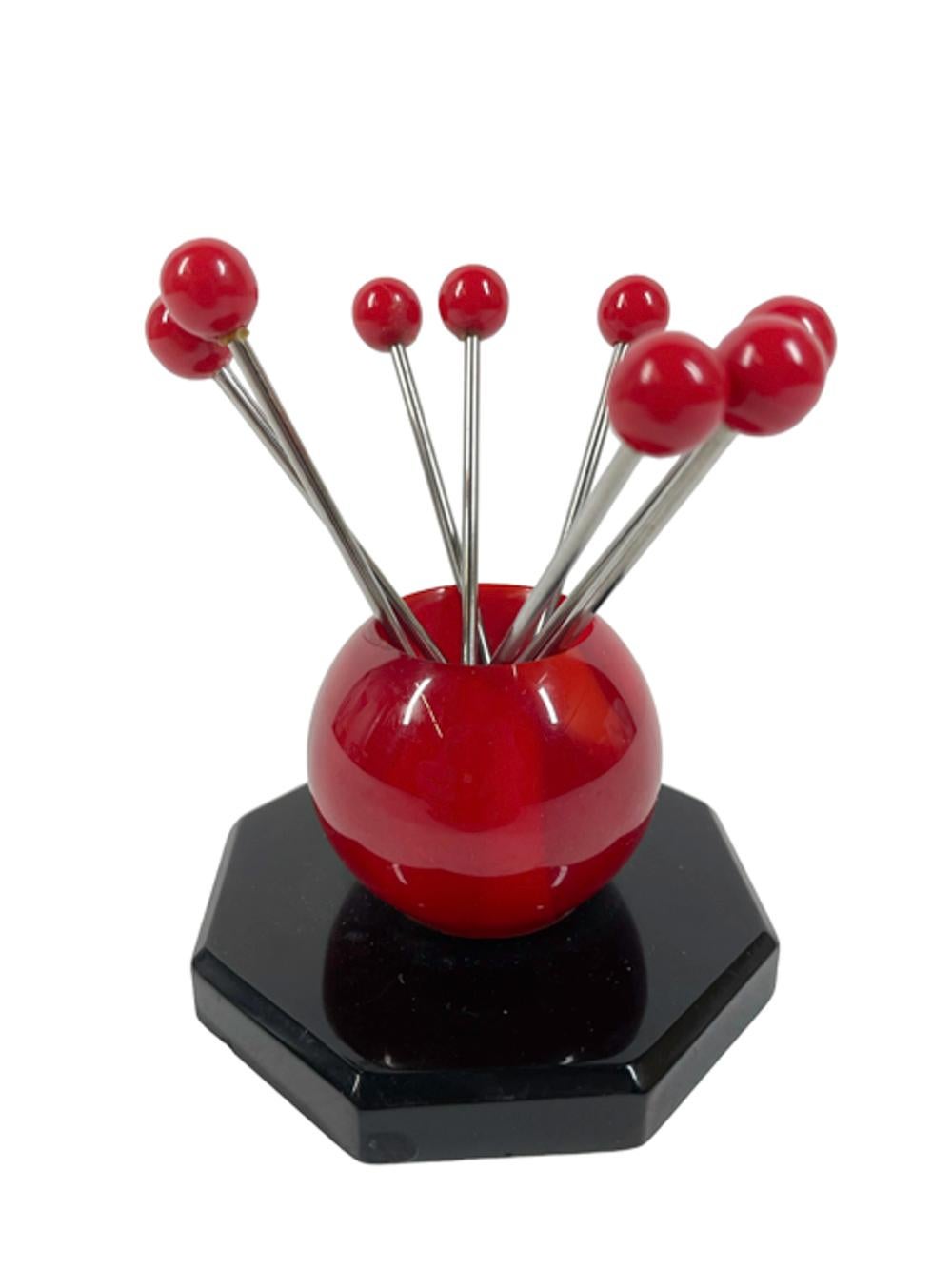 Huit pics à cocktail Art Déco à tête de boule rouge dans un support en bakélite représentant une boule rouge sur une base octogonale noire.