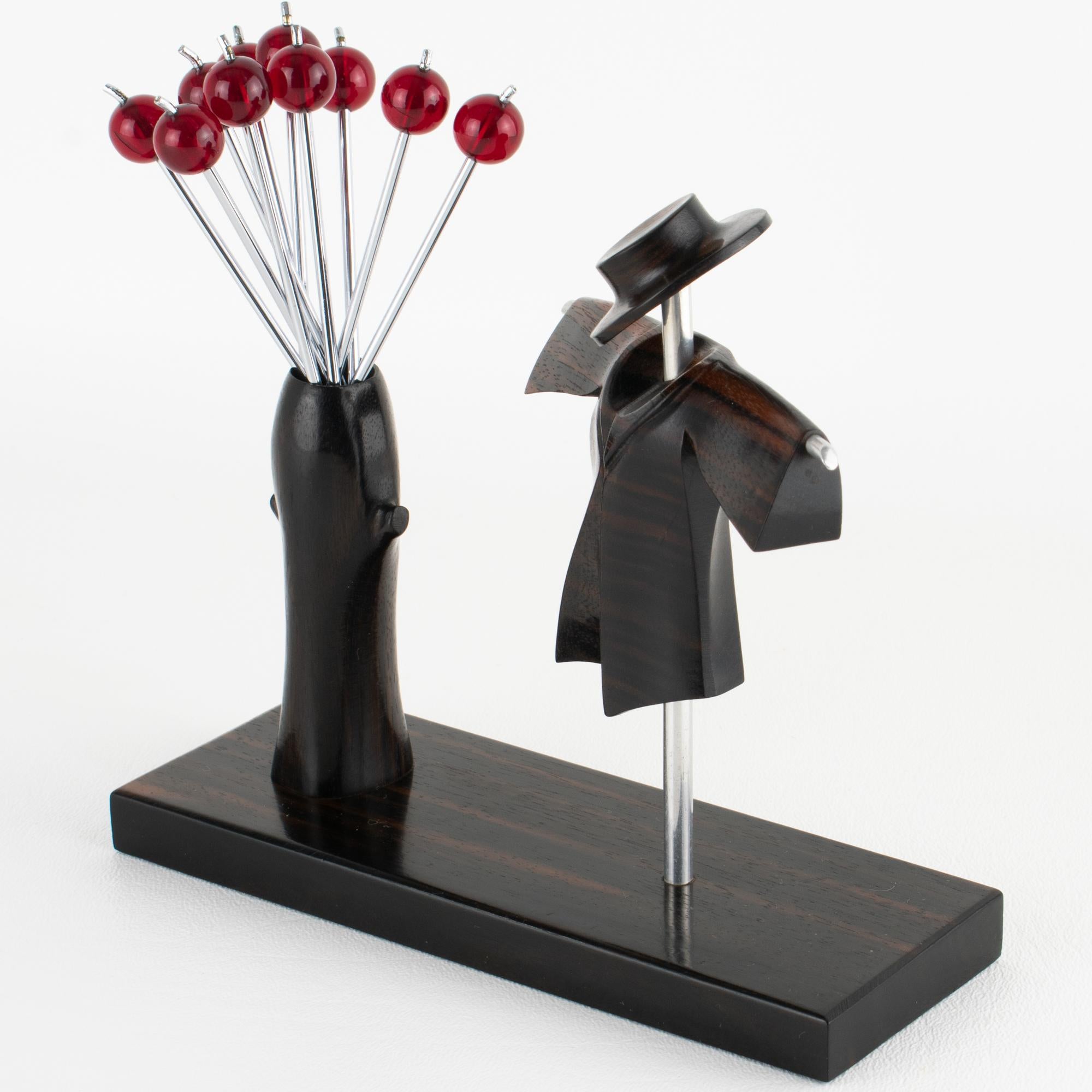 This stunning barware set, featuring a cocktail picks set, was crafted in France circa 1930. The bar set features a Macassar wood and chrome carved scarecrow facing a stylized carved wood tree turned into a fork holder. The hollow tree holds ten