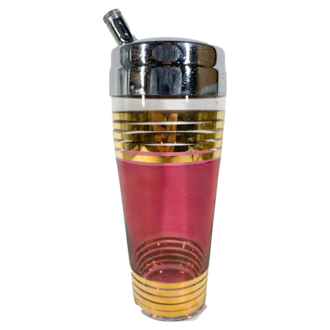 Clear glass Art Deco cocktail shaker with a wide flashed ruby red band centered between two groups of 22k gold bands and with a chrome lid.