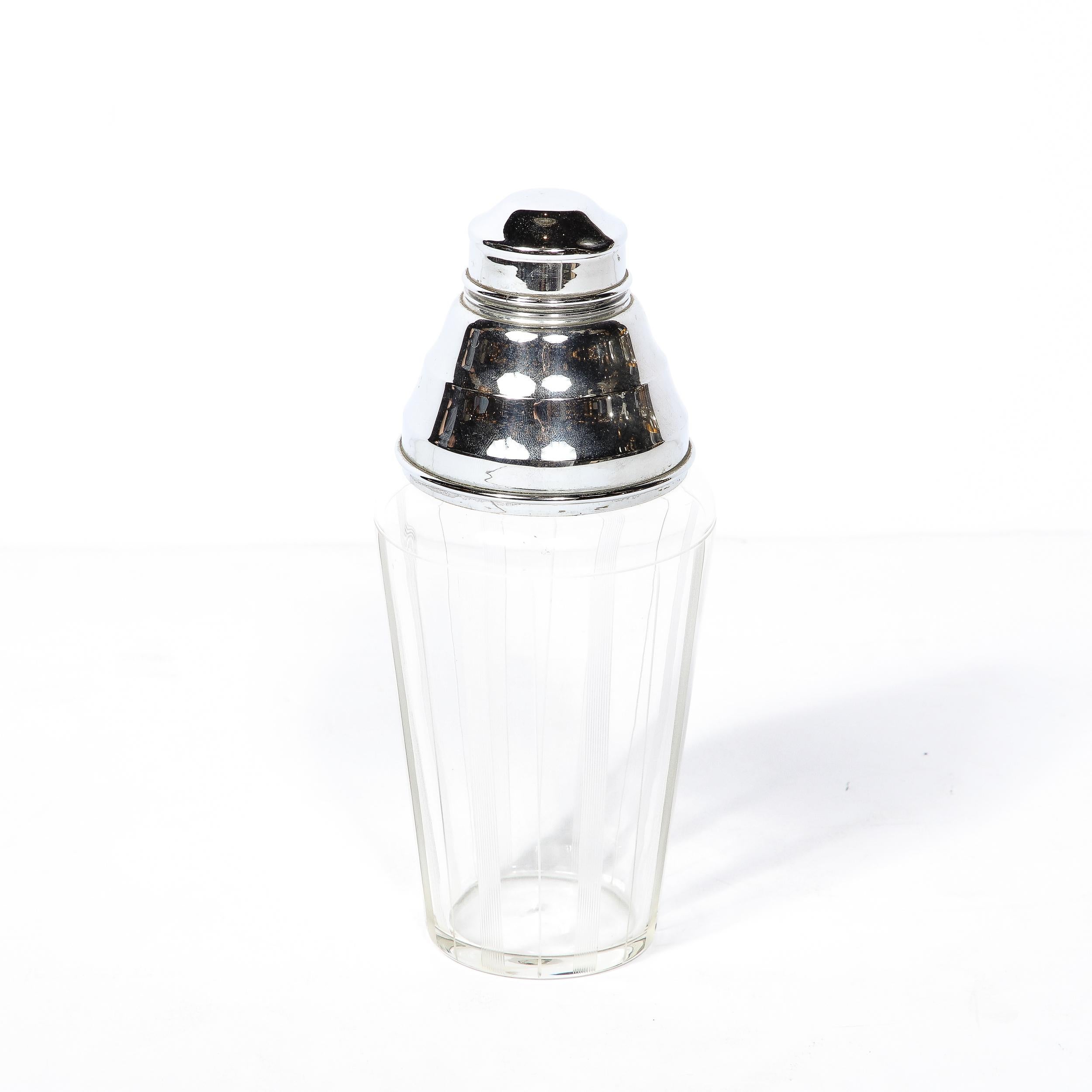 A gorgeous Art Deco Cocktail Shaker in Chrome, this piece was Made in the United States Circa 1935. It features a streamlined Chrome Strainer and Lid with a Glass Body accented with vertically etched fluted detailing in transparent glass. This