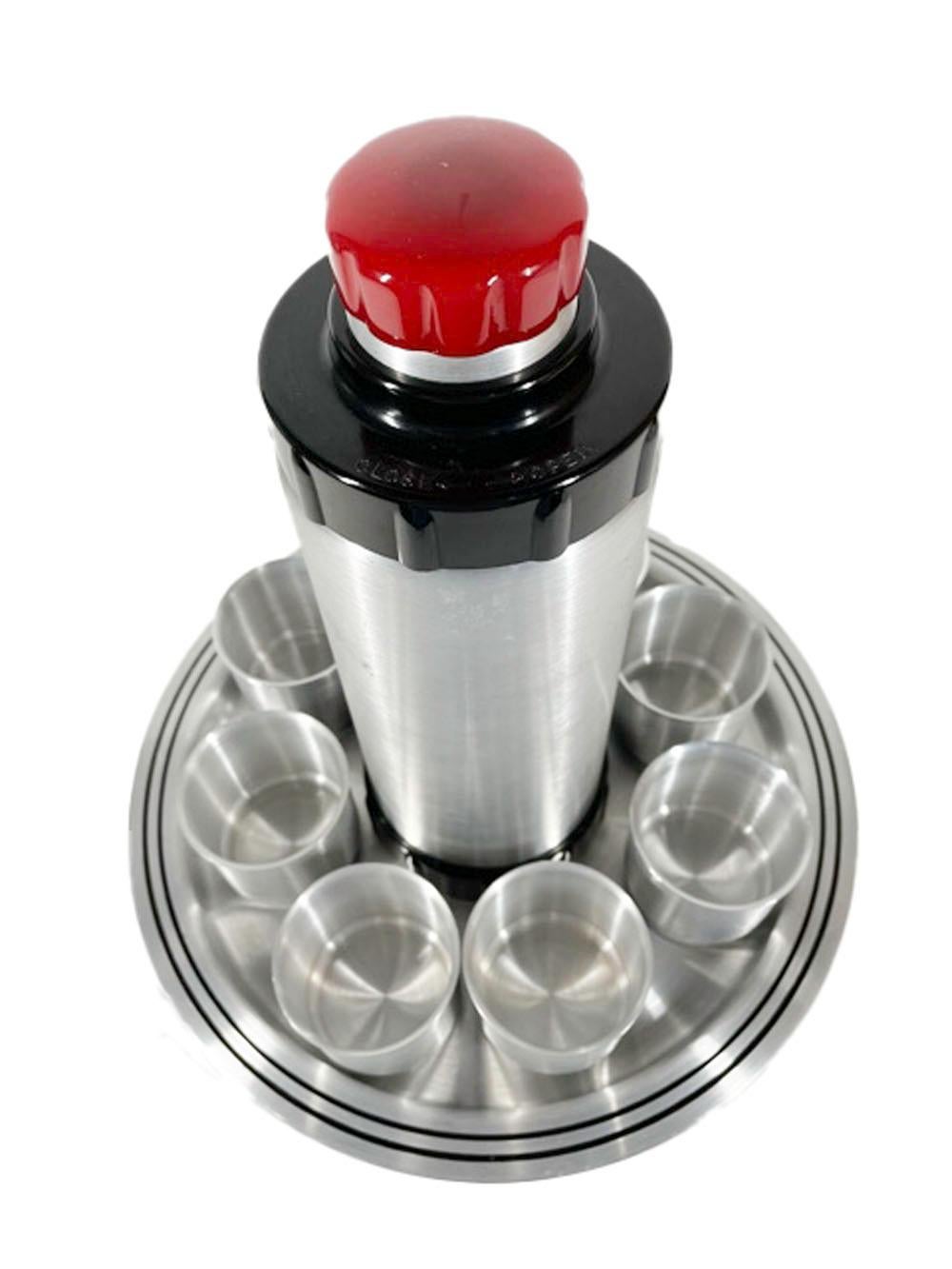 Art Deco period brushed aluminum and Bakelite cocktail shaker set. The shaker with a black Bakelite foot and screw top with a red Bakelite and aluminum cap which doubles as a jigger, while the accompanying tray and cups are decorated with an inset