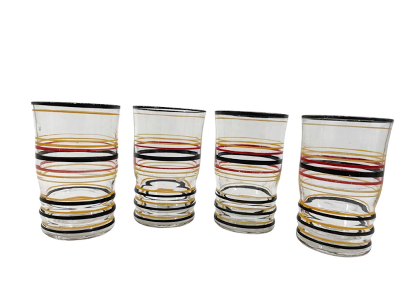 Art Deco cocktail shaker and glasses of clear optically ribbed glass with molded rings and hand painted rings in black, red, orange and yellow. The shaker with a domed aluminum lid and cap with a strainer in the lid.