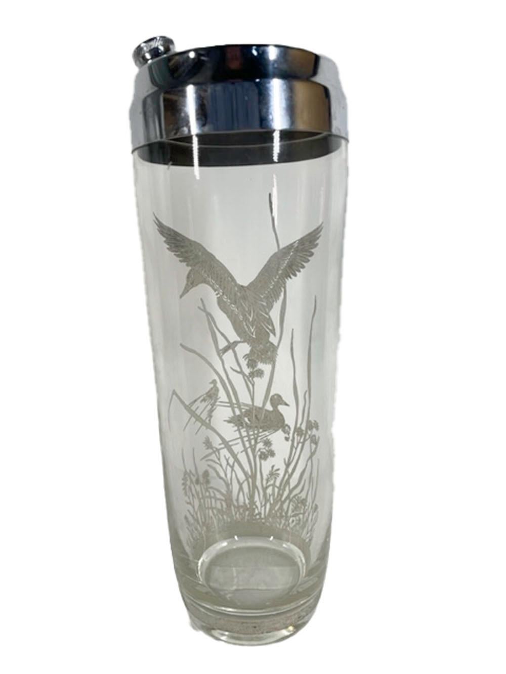 Clear glass cocktail shaker with a chrome lid and decorated with a sterling silver overlay scene of a duck landing in water with tall grass and other ducks swimming nearby.