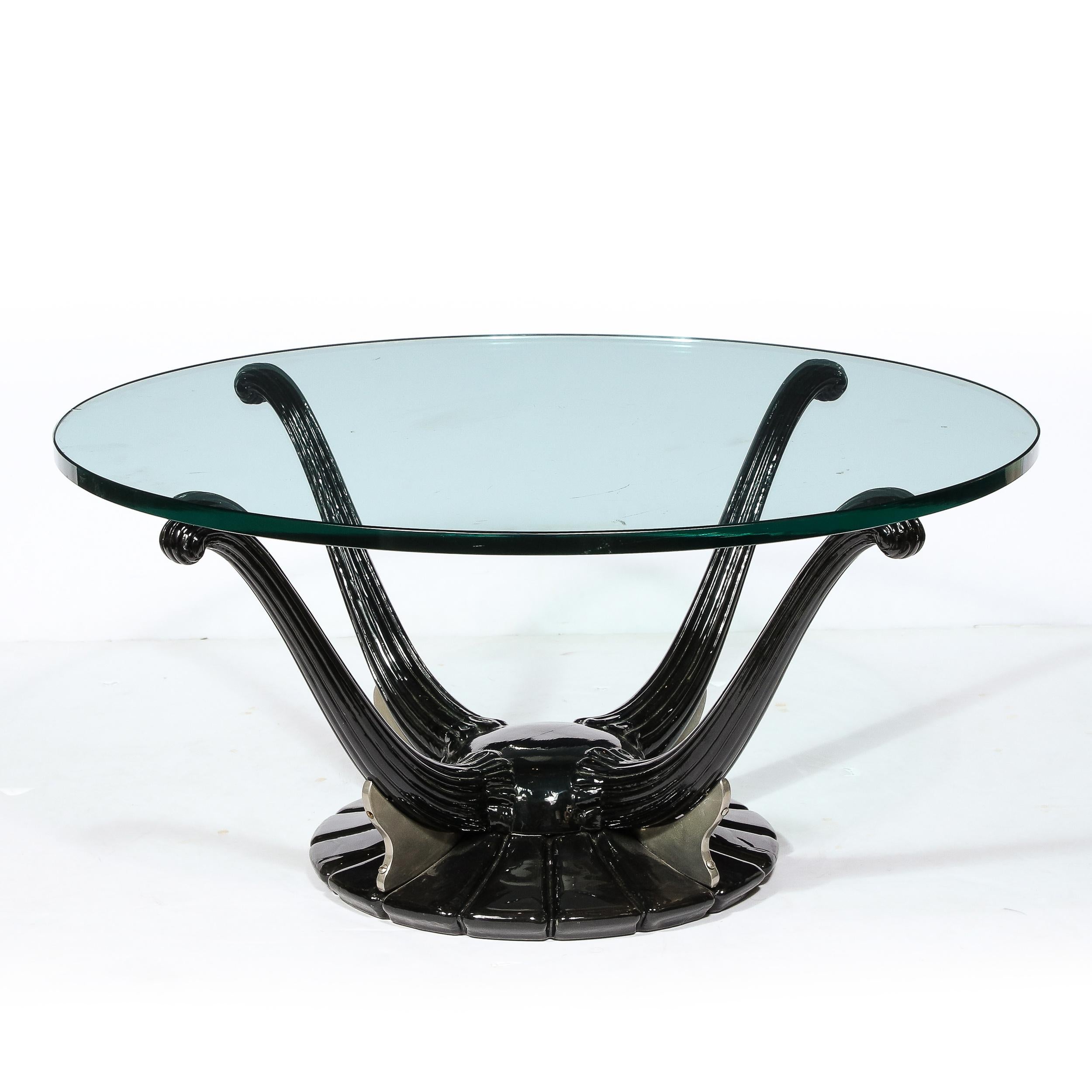 This refined Art Deco style cocktail table was realized- in the manner of Ruhlmann- in the United States during the 20th century. The piece features a graphic and stylized base consisting of four scroll form fluted tendrils that extend out