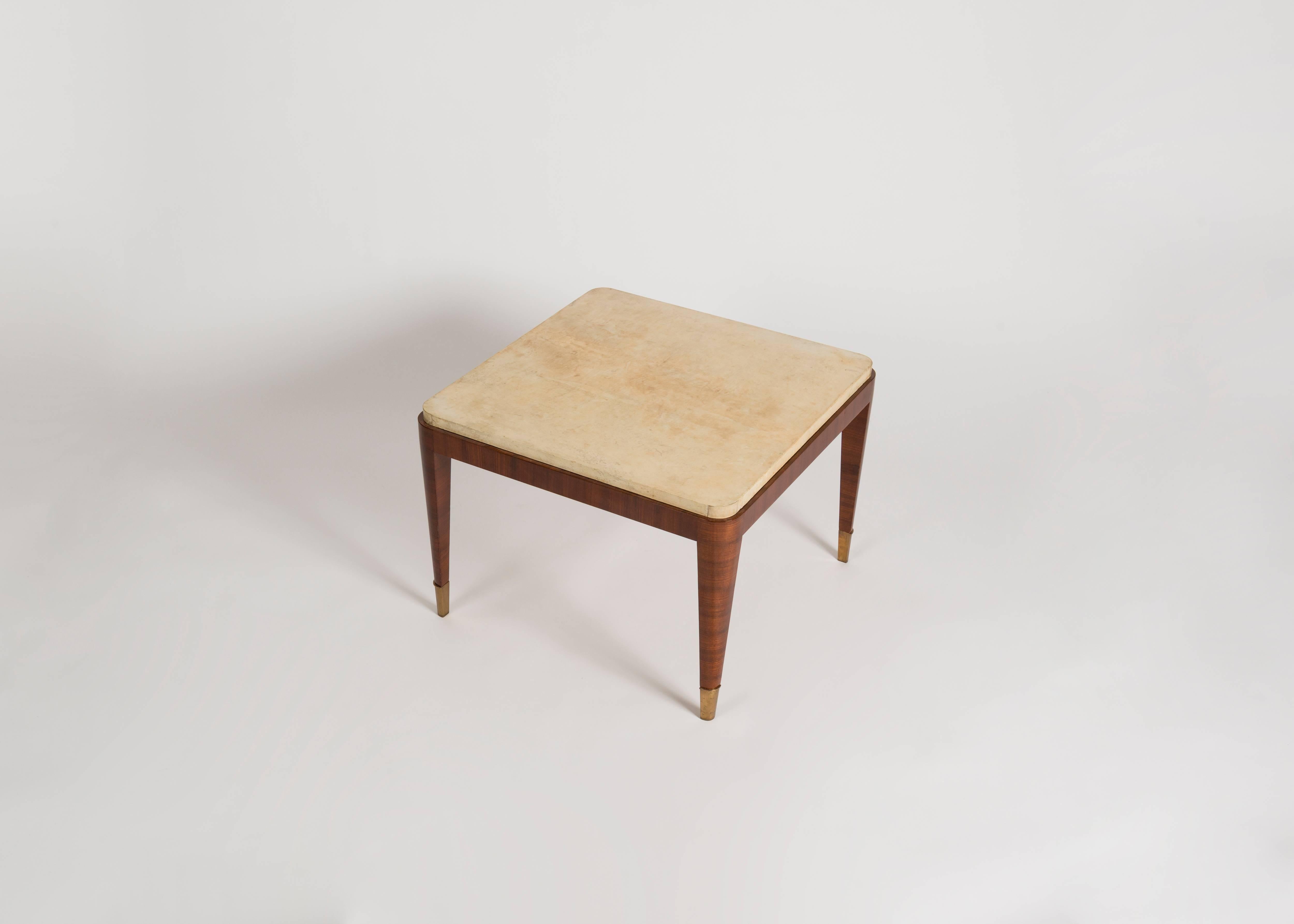 This deco coffee table in striped mahogany, featuring gilt bronze sabots and a lush parchment top, is remarkable for its fine legs, geometric top, rounded corners, and altogether subtle and delicate proportions. The parchment top is a probable