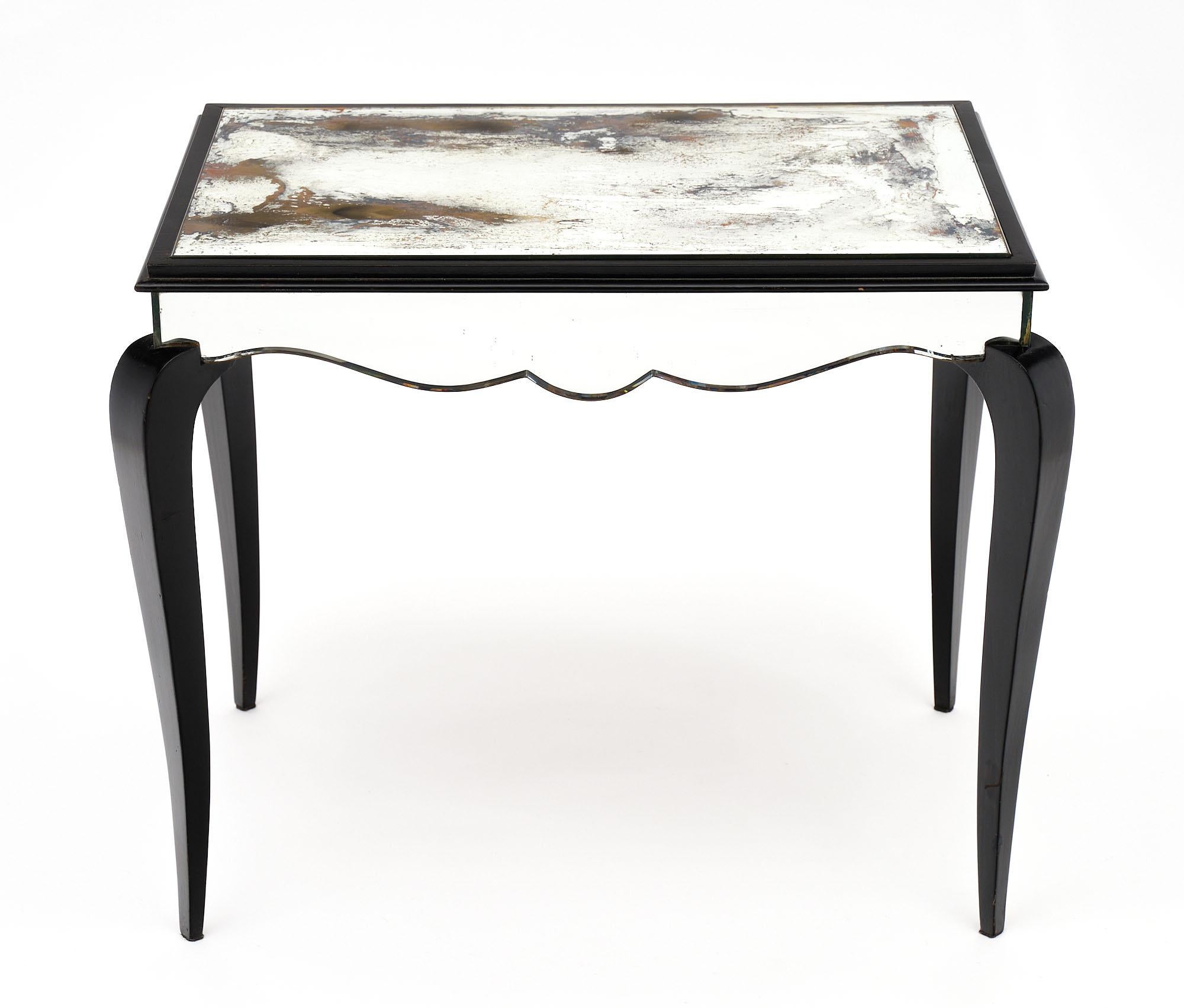 French Art Deco period coffee table, strongly attributed to Dominique. This piece has a beautiful heavily antiqued mirrored glass top. The apron features scalloped edges and is also mirrored. The curved legs are finished with an ebonized museum