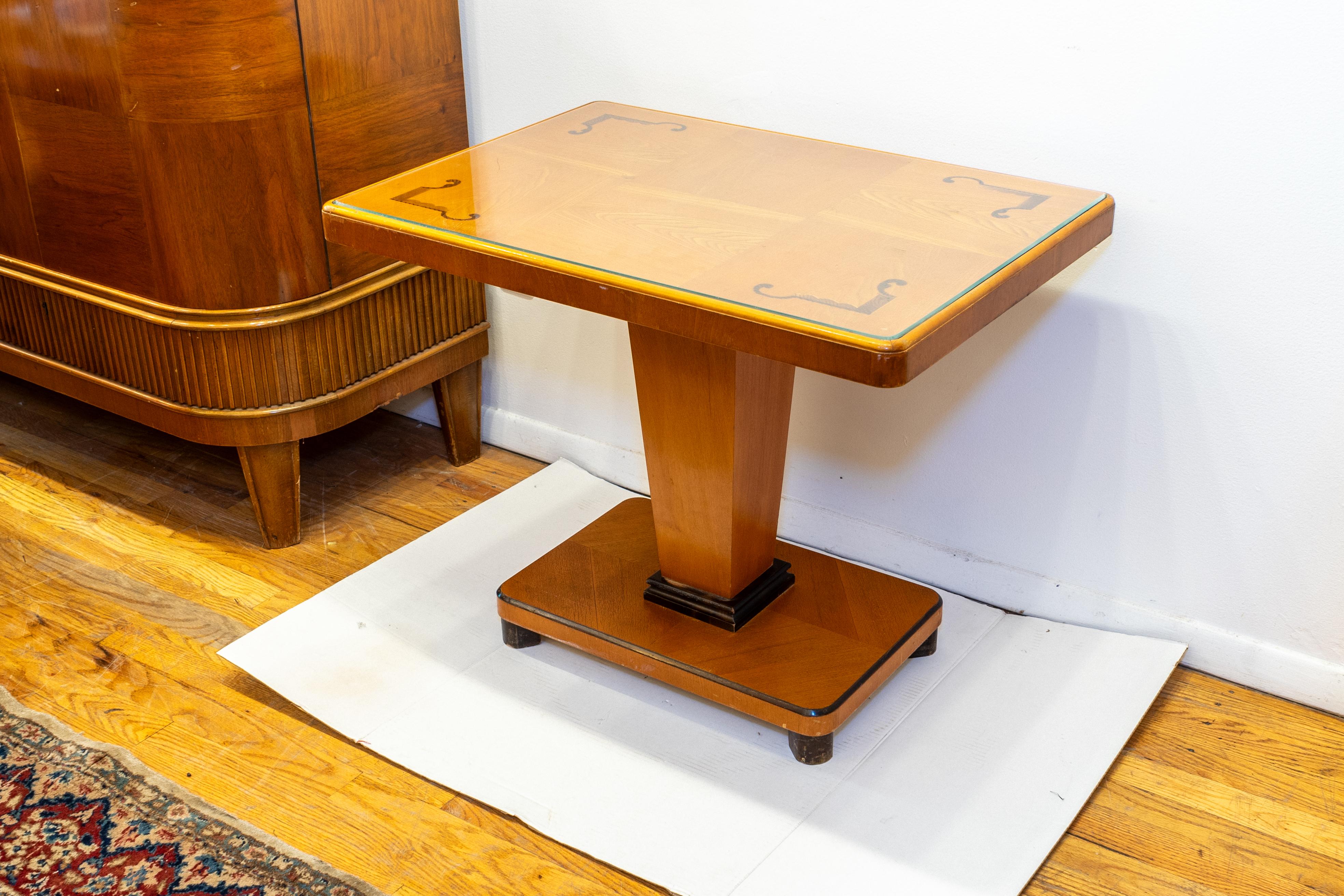 A pedestal style coffee table constructed of solid Swedish Ash, and veneered in bookmatched Ash face sections. It is inlaid with a stylized Art Deco motif in Walnut. The feet and elements of the base are stained and lacquered a Walnut tone as well. 
