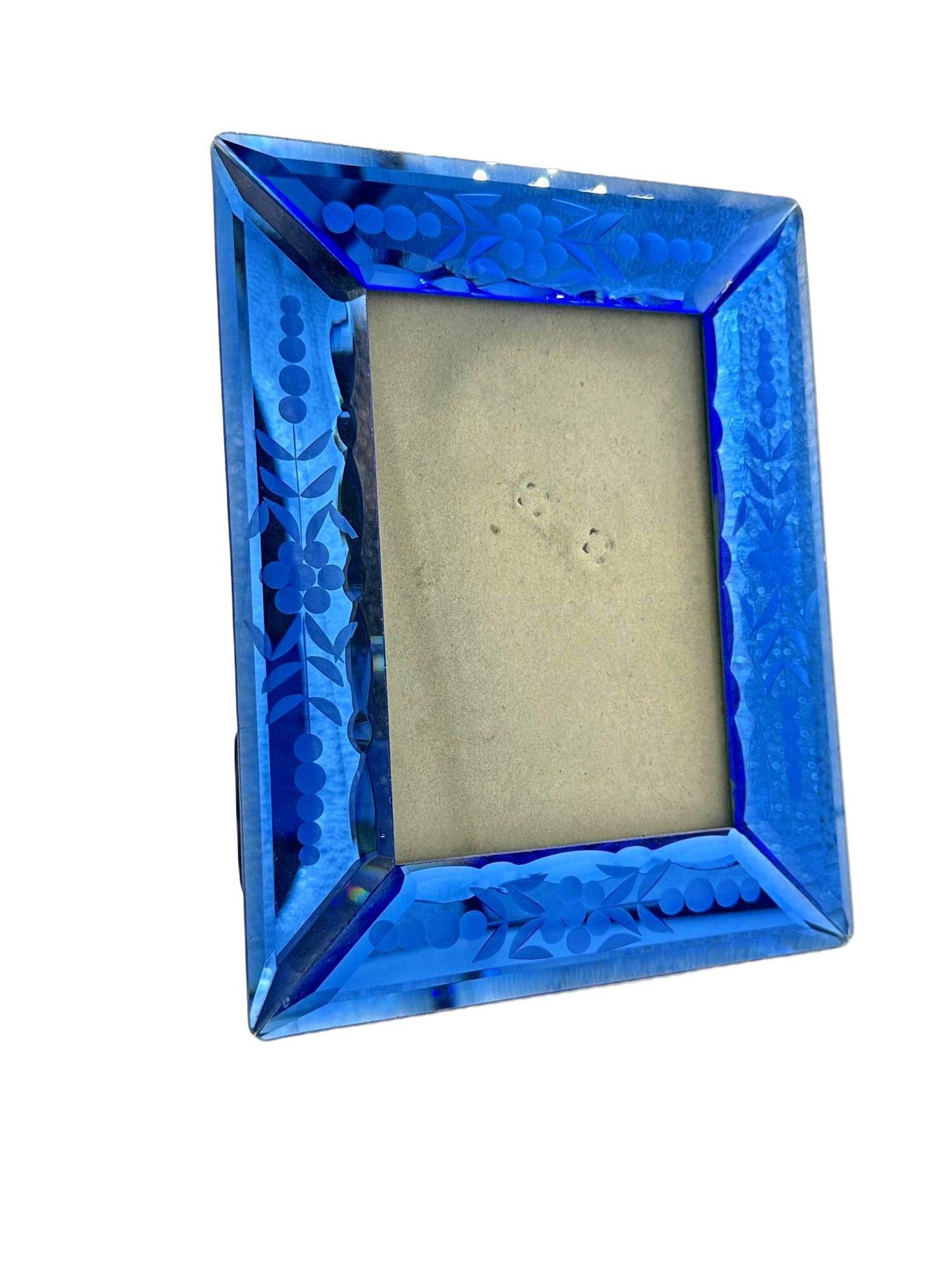 A vintage cobalt blue glass picture frame with floral etchings, Cobalt blue is a vibrant and intense blue, reminiscent of the deep blue color of cobalt salts. It has a rich and saturated appearance, often described as bold, striking, and vivid. When