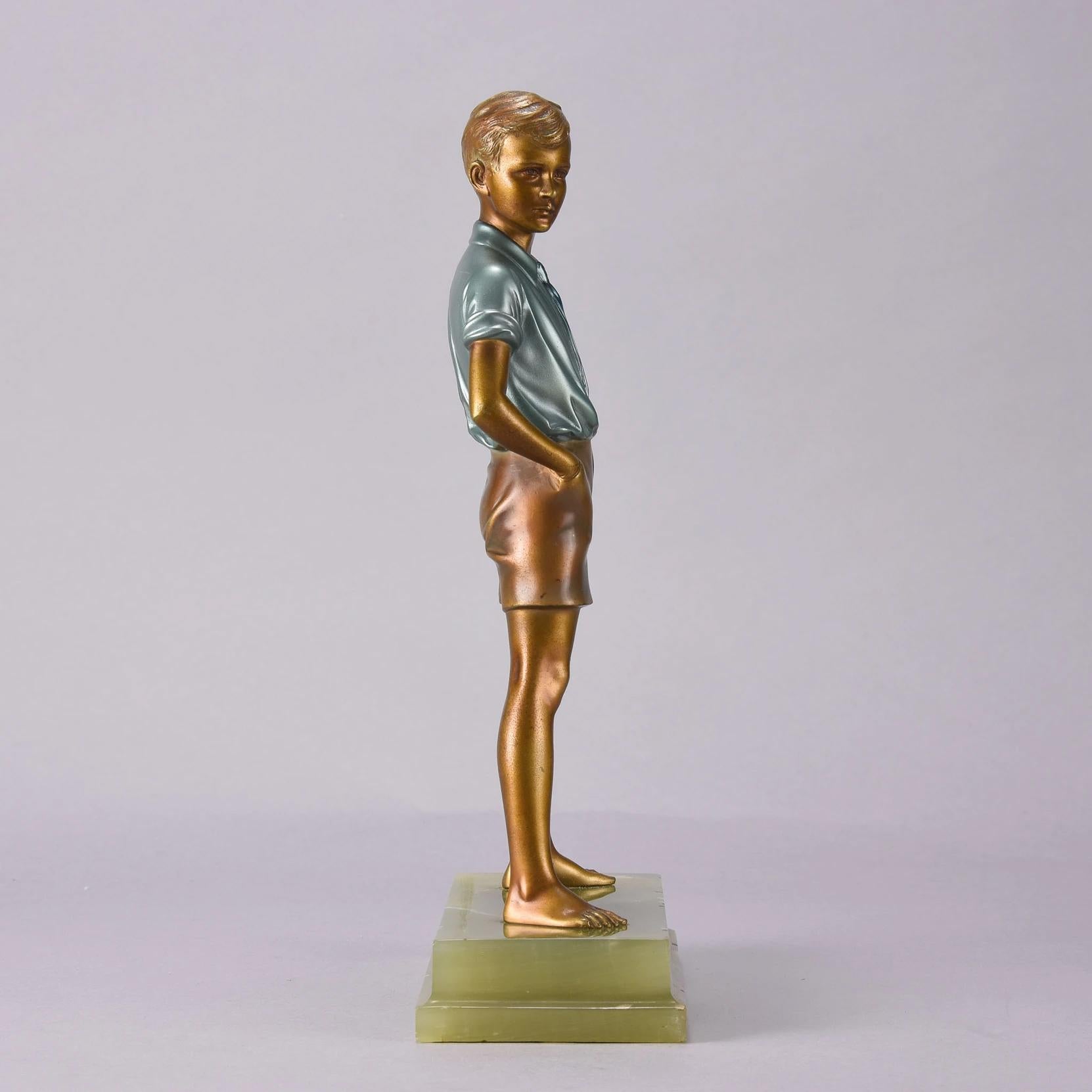 An excellent early 20th century Art Deco cold painted bronze figure of a young boy in shorts holding a book under his arm with his hands in his pockets. The bronze has excellent cold painted metallic enamel color and is raised on a rectangular