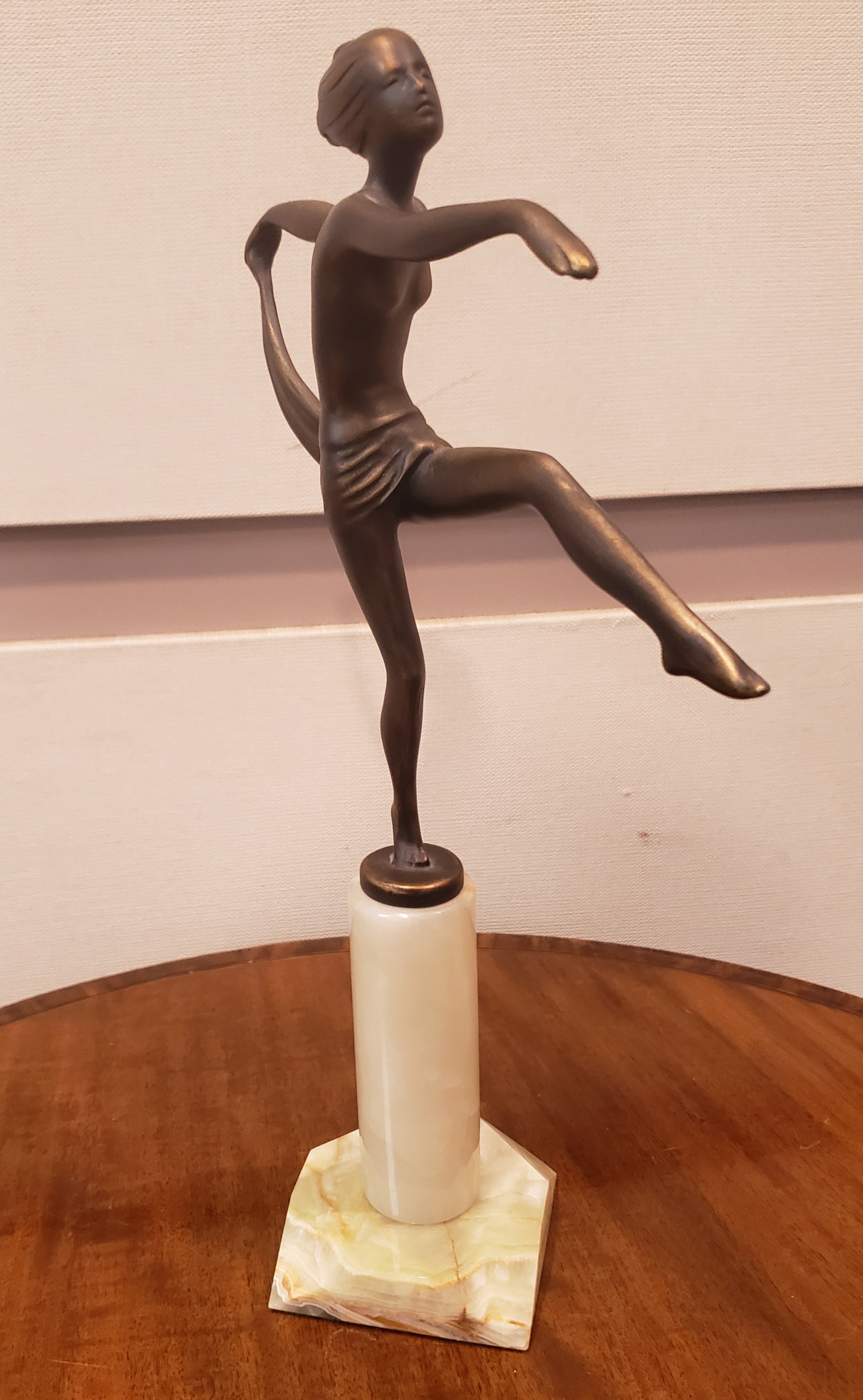 An attractive 20th Century Art Deco cold painted bronze figure of a naked dancer with her arms outstretched in an elegant pose holding the hem of the scarf that is draped around her waist with one leg kick out infront of her. The sculpture exhibits