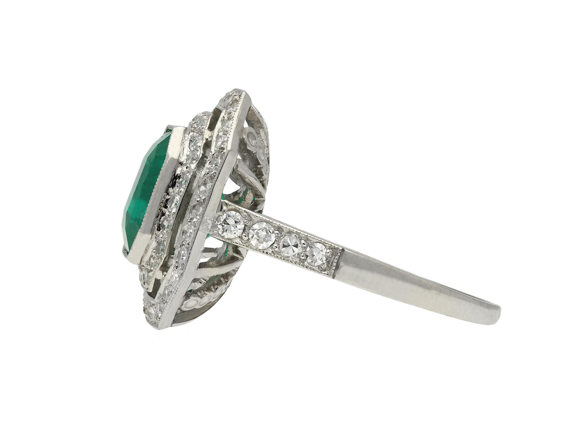 Art Deco Colombian emerald and diamond cluster ring. Set to centre with an octagonal step cut natural Colombian emerald with no colour enhancement and minor clarity enhancement in an open back rubover setting with an approximate weight of 3.20