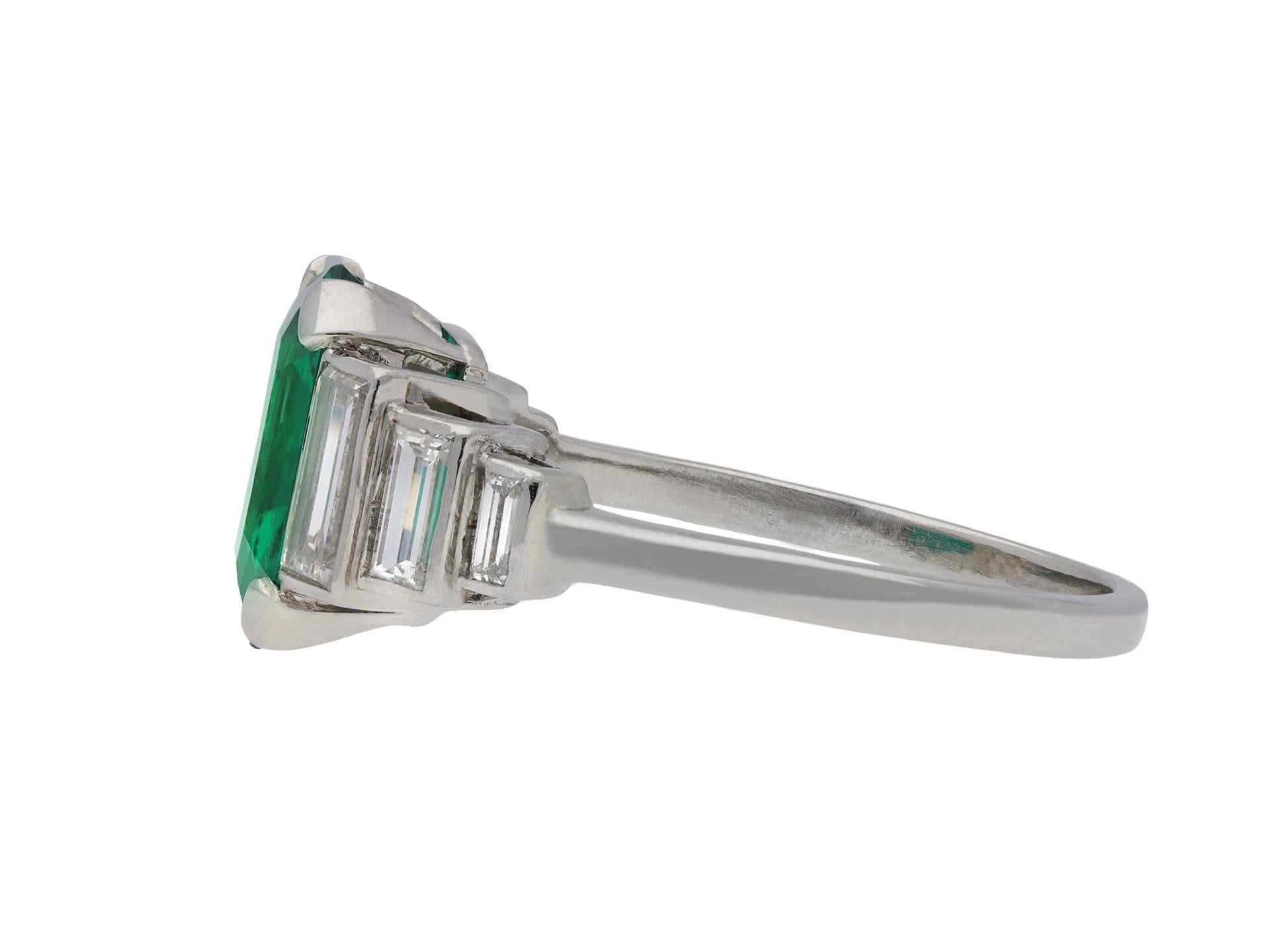 Art Deco Colombian emerald and diamond flanked solitaire ring. Centrally set with an octagonal step cut natural Colombian emerald with minor clarity enhancement, in an open back claw setting with an approximate weight of 2.55 carats, flanked by six