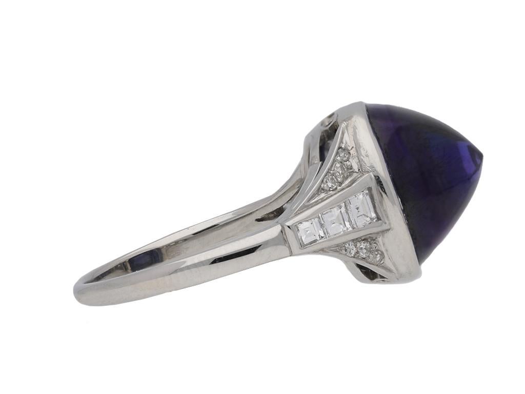 Art Deco colour change sapphire cabochon ring. Set to centre with a sugar loaf cabochon natural unenhanced Ceylon blue/purple colour change sapphire in an open back rubover setting with an approximate weight of 10.14 carats, flanked by six square
