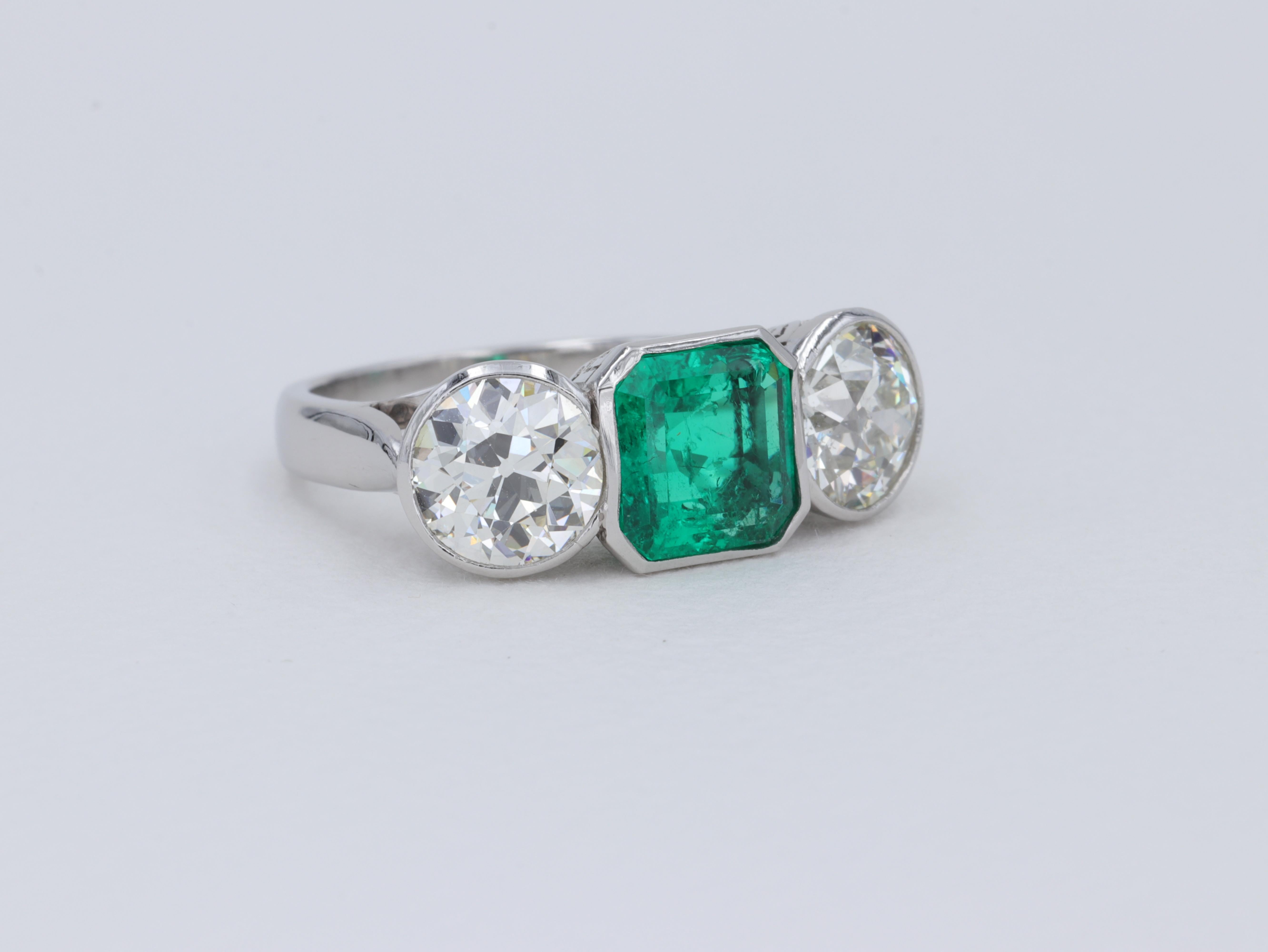 This magnificent art deco three stone ring hand crafted in platinum features a beautiful 2.14 carat Colombian emerald of top color with insignificant to minor traditional oil present as noted by its accompanying AGL report. The emerald is flanked by