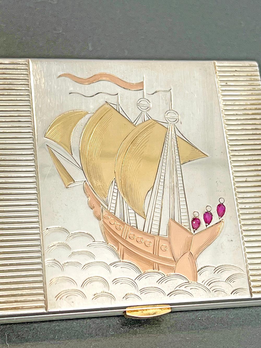 One of the most beautiful and finely crafted Art Deco compacts we have seen, this example is made from silver highlighted with gold, rose gold and rubies, and depicts a sailing ship on the high seas engraved into the lid of the compact. This piece