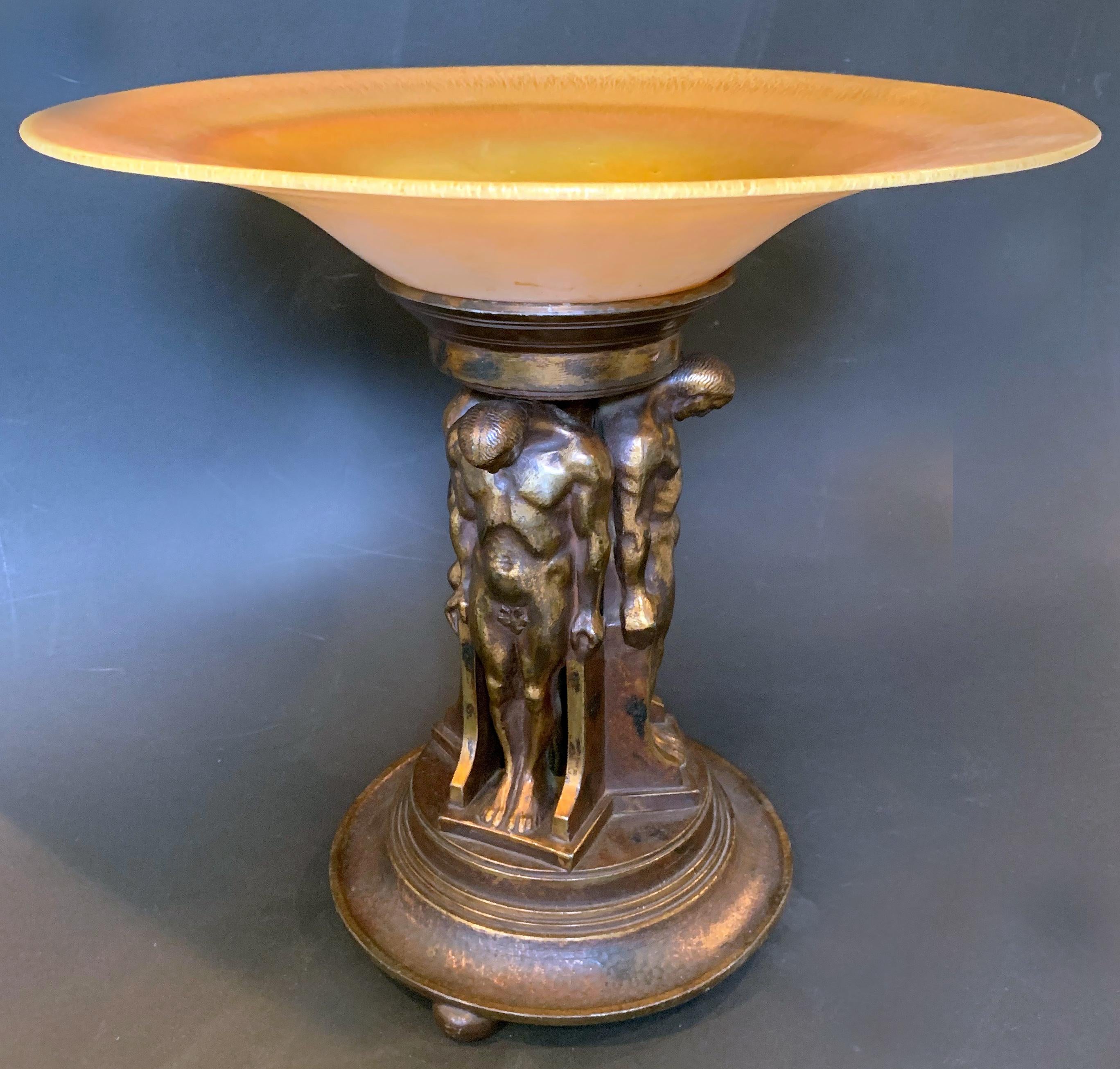Stunning in design and execution, this large Art Deco compote is composed of a bronze base featuring a group of nude male caryatids supporting a gorgeous, gold-hued glass compote made by Lustre Glass. Oscar Bach used the nude male caryatid motif in