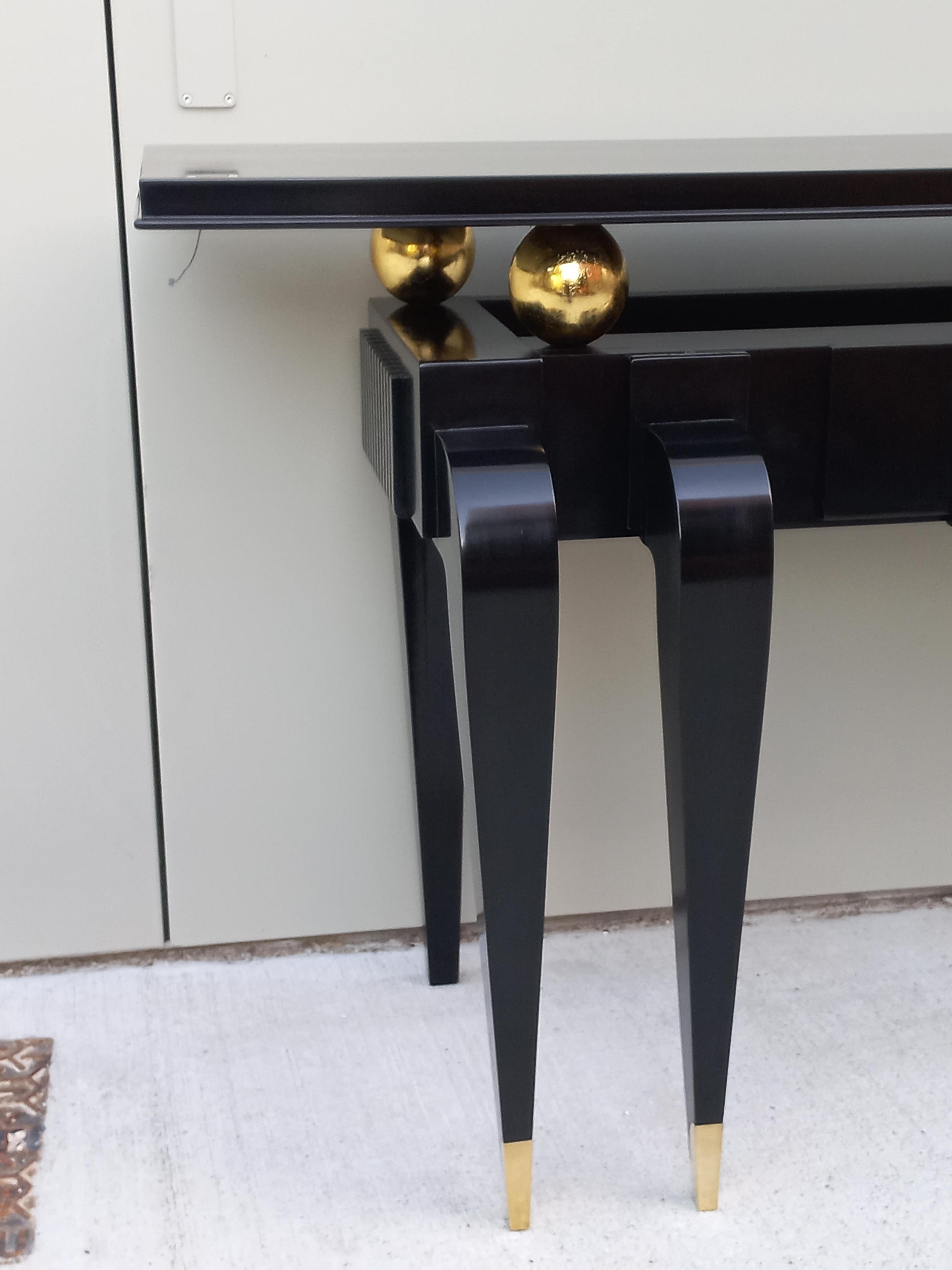 Important 1930 Art Deco architectural console in black lacquered wood and gold leaf wood. Slightly curved front legs, the bottom in brass. The large tray is underlined by a molding, it is placed on four spheres in gilded wood. (the console is
