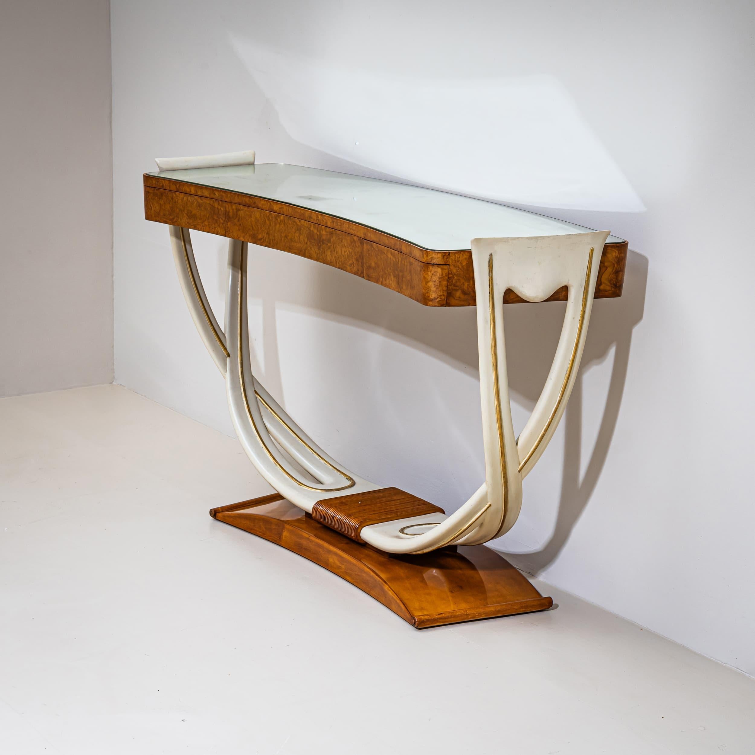 Art Deco console table featuring a U-shaped white-lacquered frame and walnut burl veneer on the front. The piece includes three drawers and a mirrored glass top showing charming age-related clouding. The frame is gold-patinated and rests on a curved