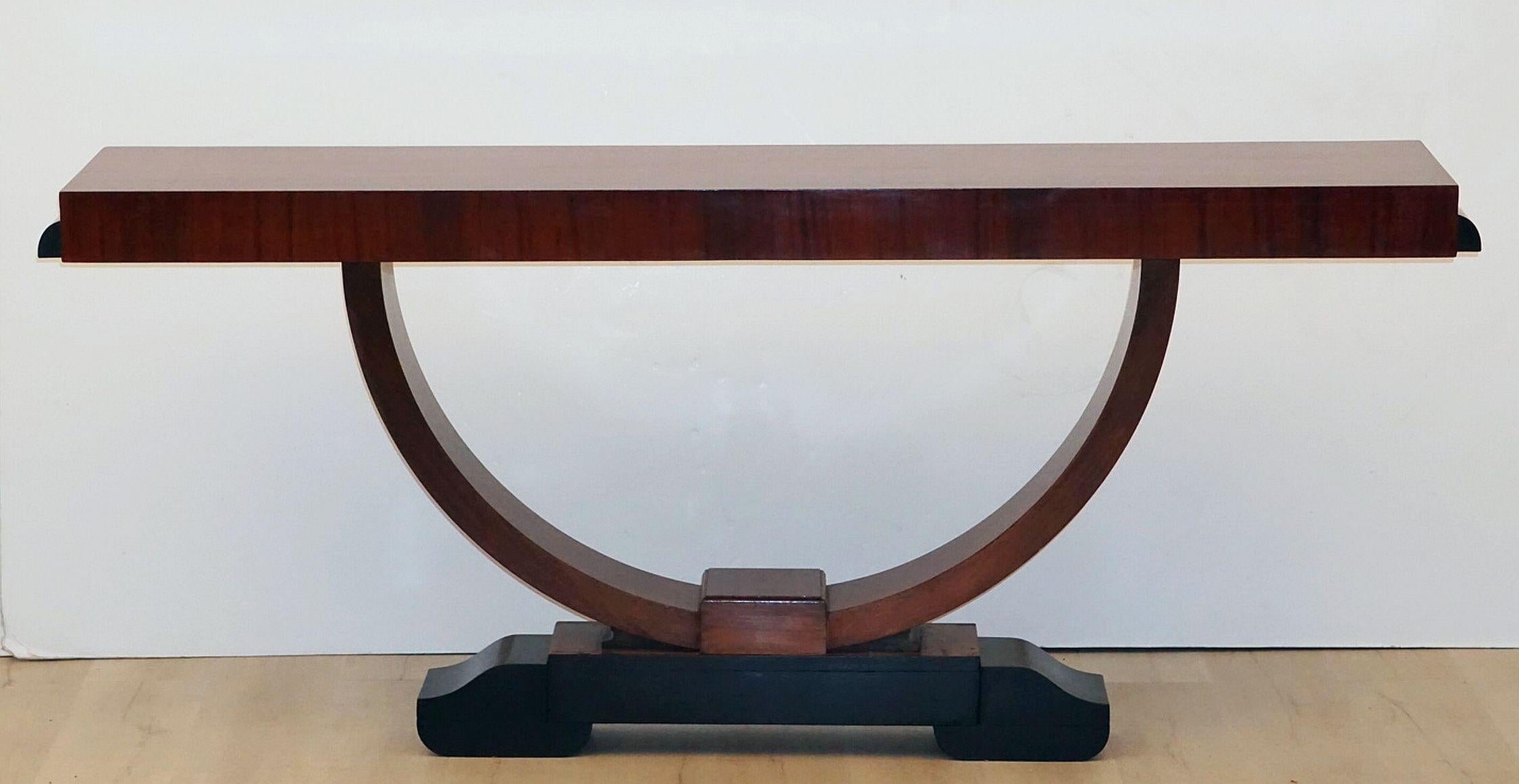 A fine English console table in the Art Deco style, featuring a rectangular top of mahogany set upon a half ring support, mounted to a shaped raised base of ebonized wood.

